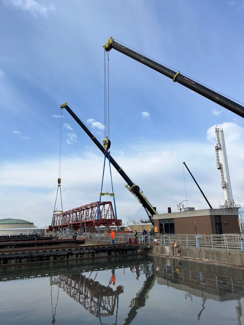 Two cranes are working on a bridge over a body of water