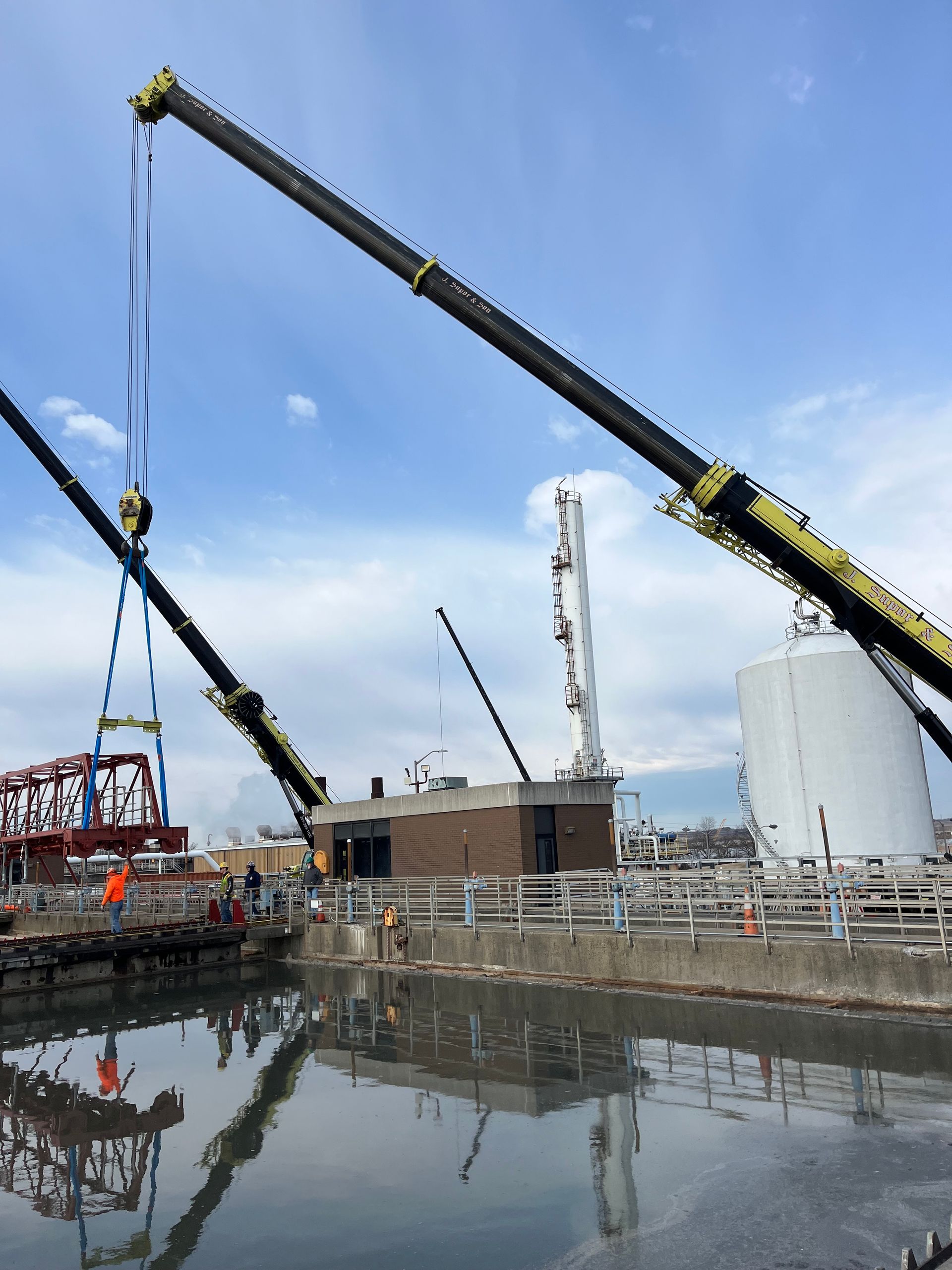 Two cranes are lifting a bridge over a body of water