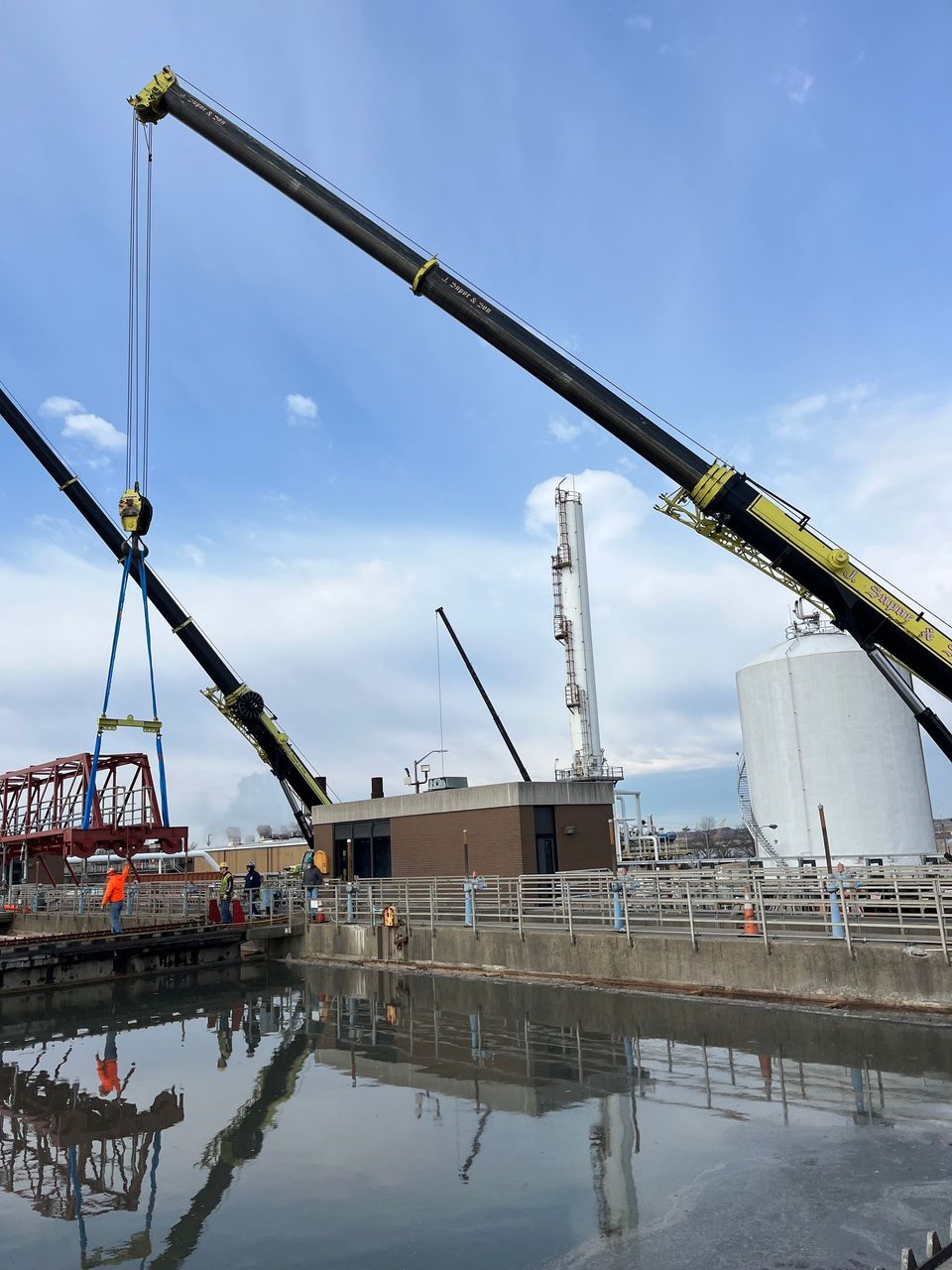 Two cranes are lifting a bridge over a body of water