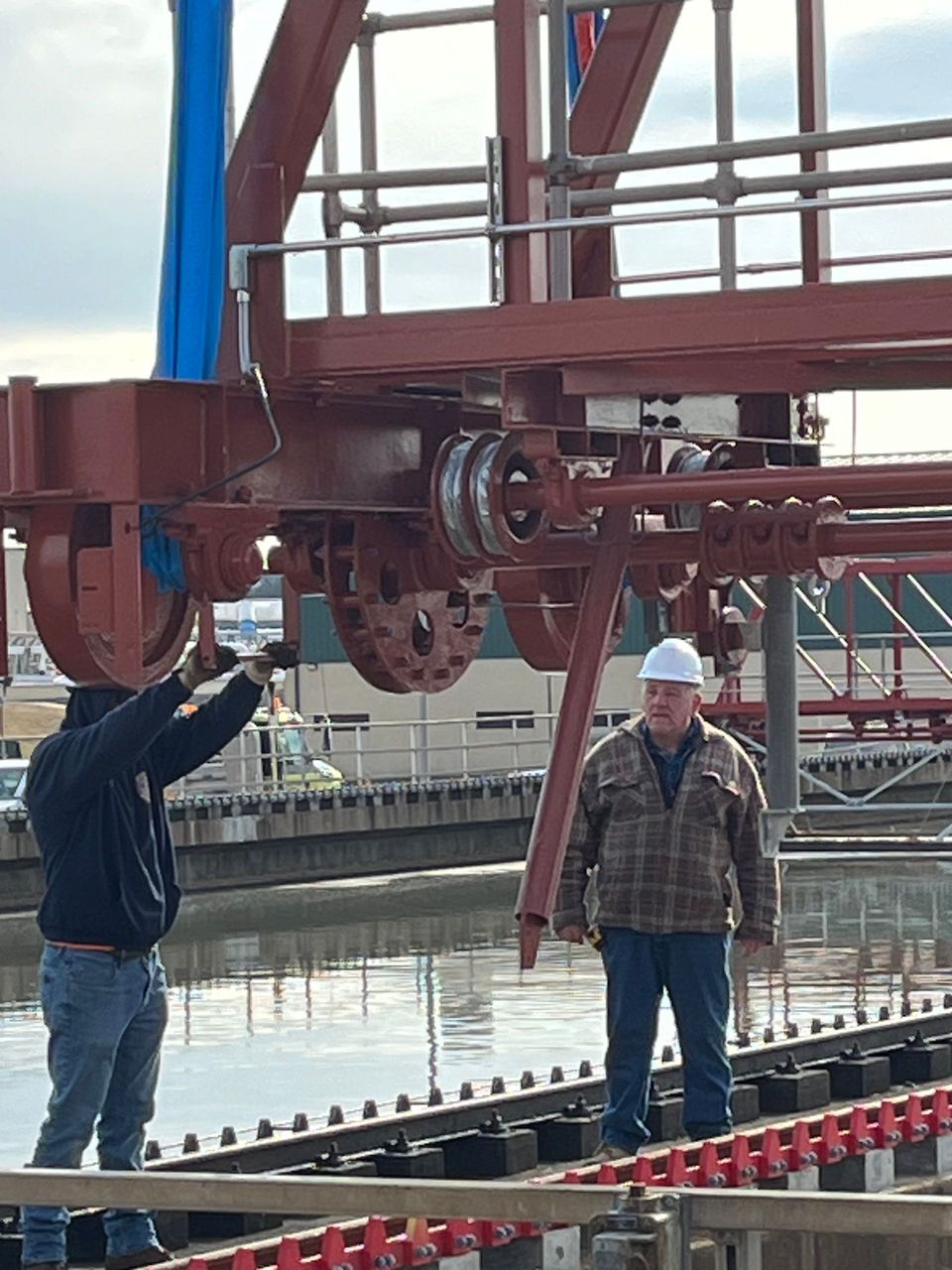 Two men are working on a large metal structure near a body of water.