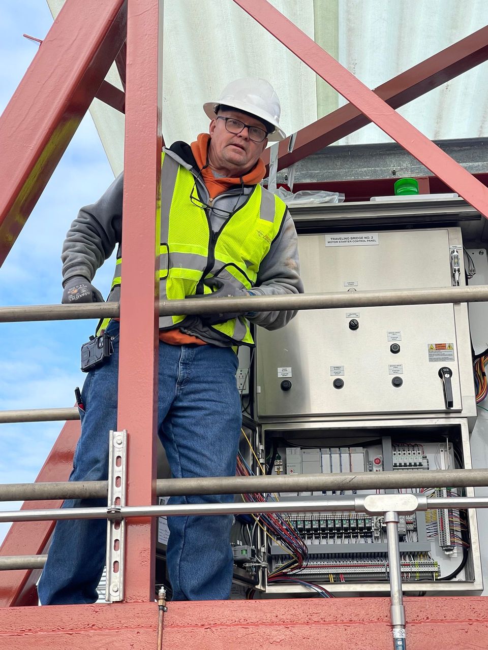 A man wearing a hard hat and safety vest is standing on top of a metal structure