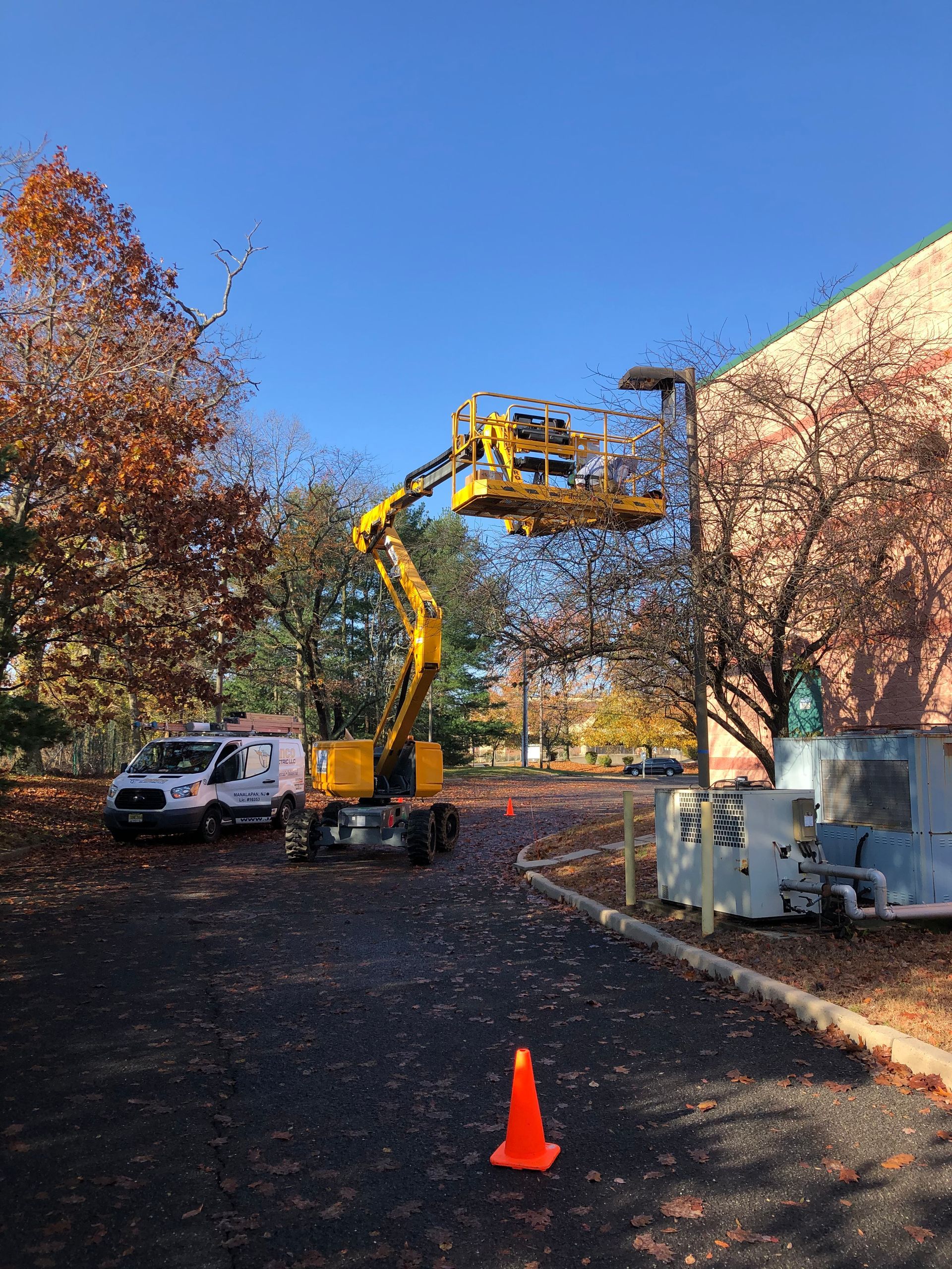 A yellow crane is lifting a light pole in a parking lot.