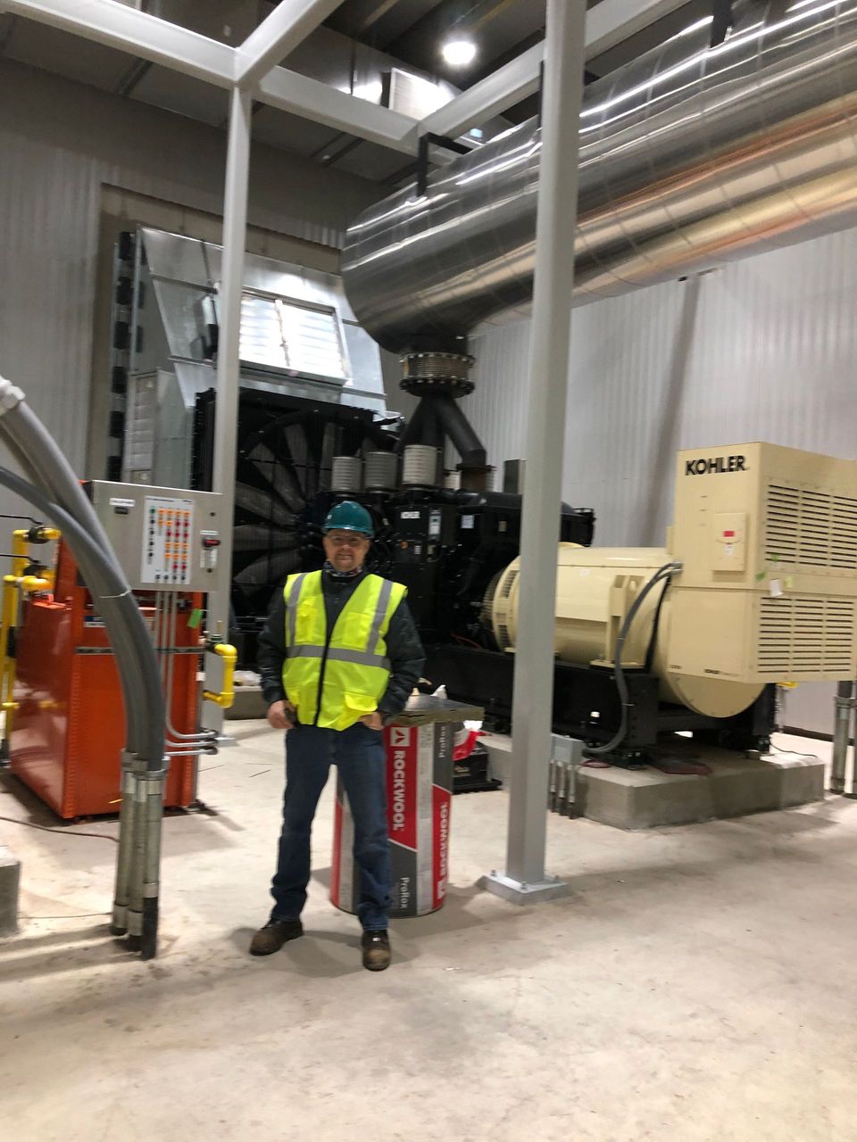 A man in a yellow vest is standing in a room next to a machine.