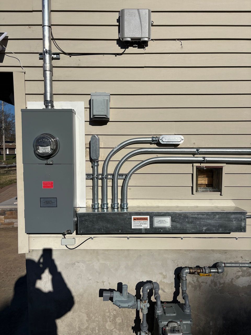 Electrical meter and service panel on beige building exterior with conduit and small utility boxes.