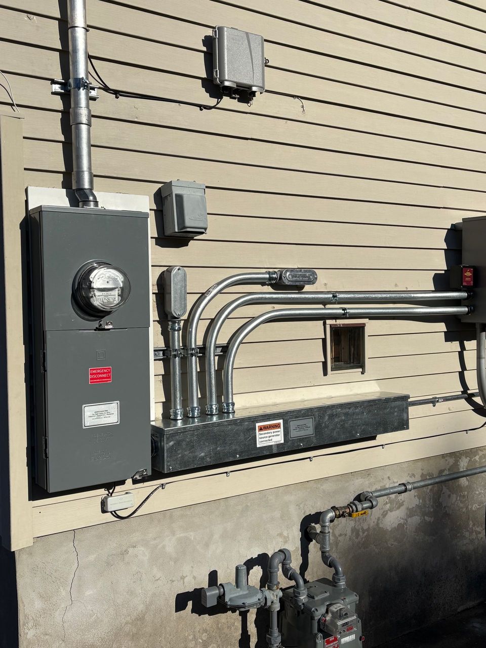 Exterior electrical meter and conduit mounted on a beige building wall.