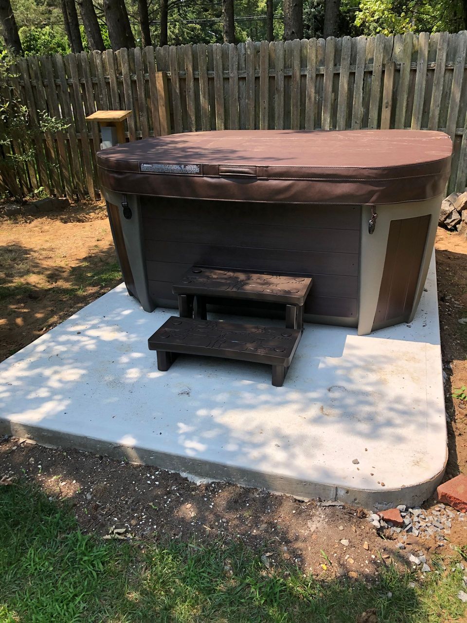 A hot tub is sitting on top of a concrete platform in a backyard.