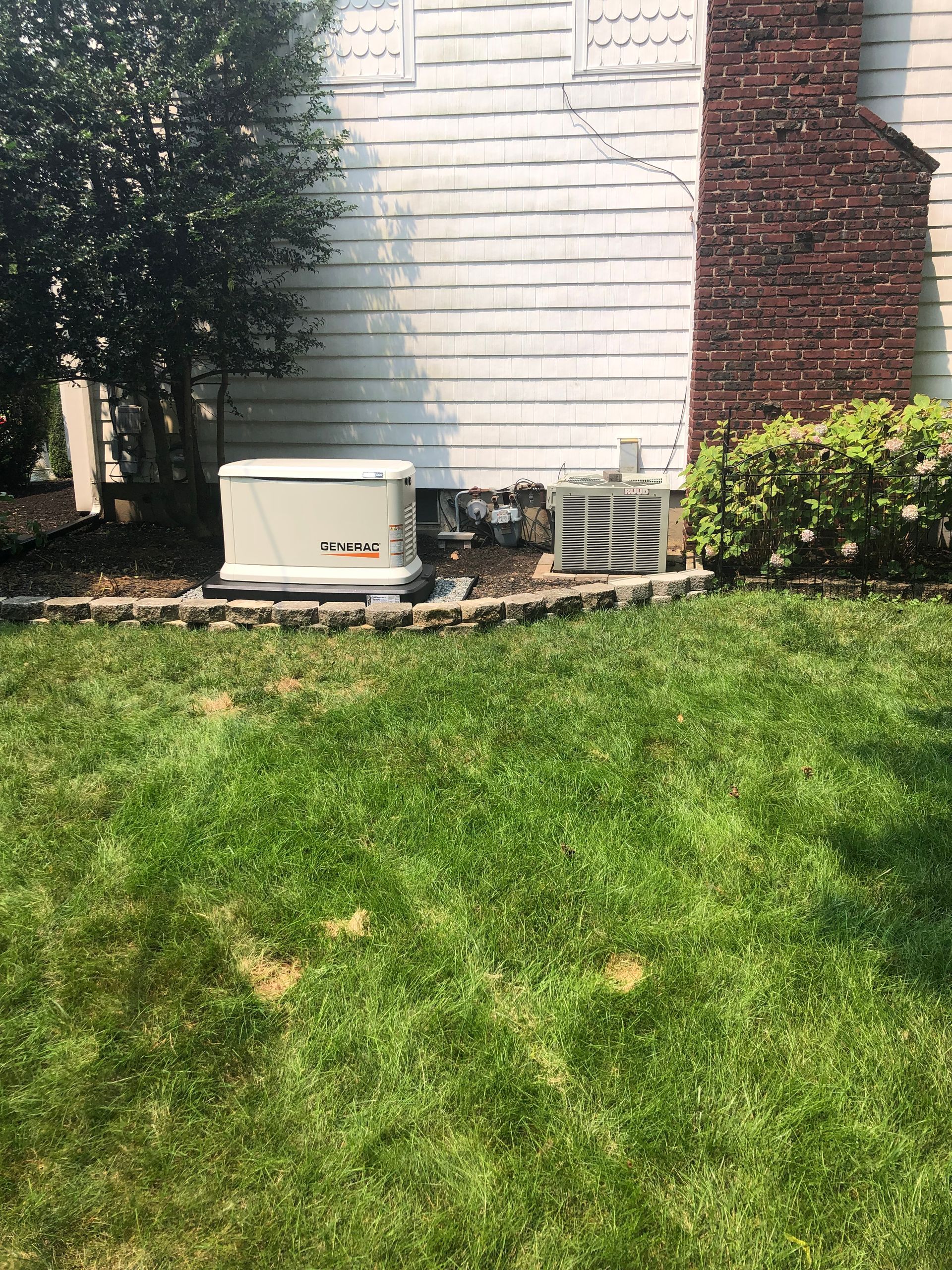 A generator is sitting in the grass in front of a house.