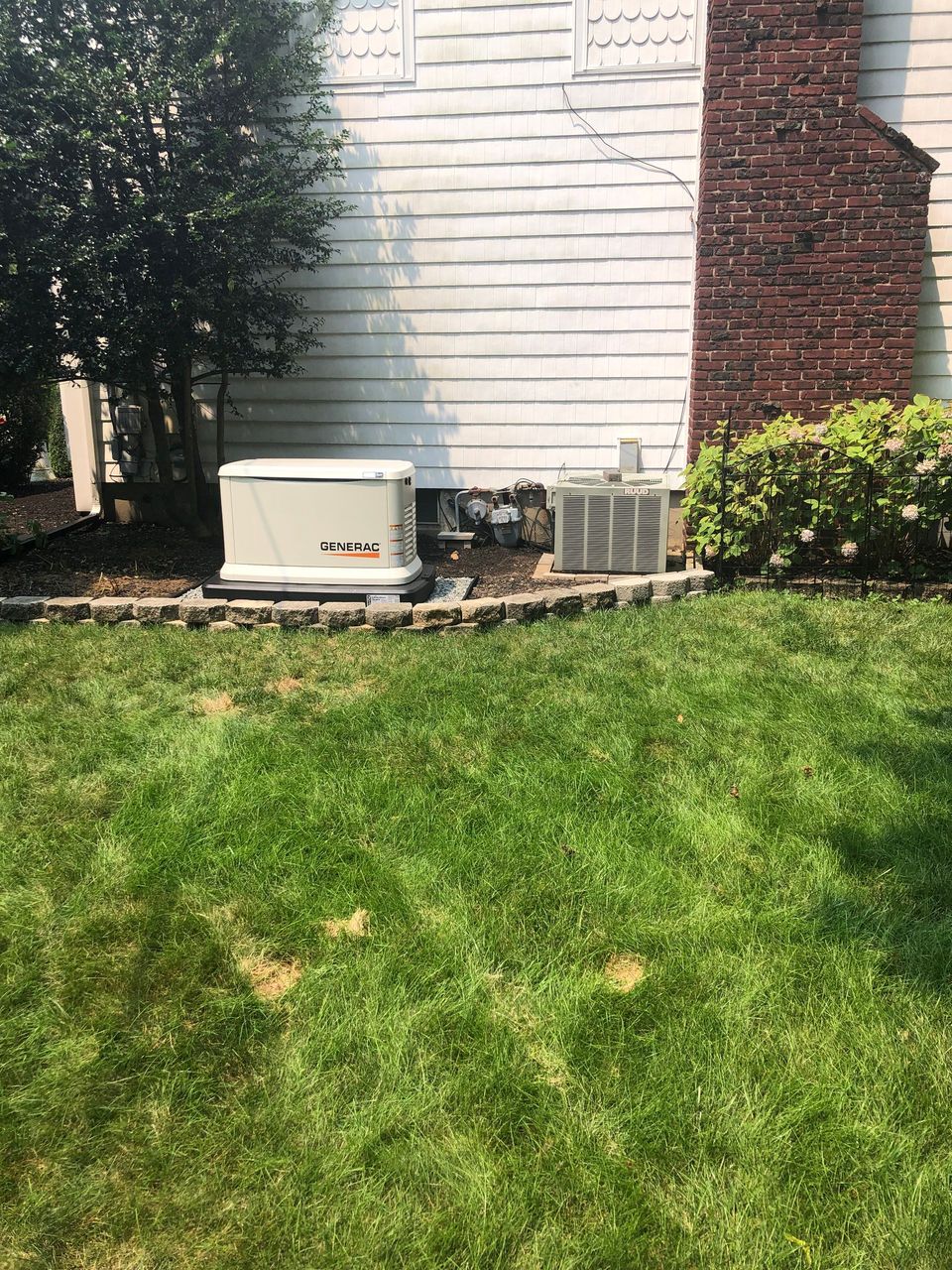 A generator is sitting in the grass in front of a house.