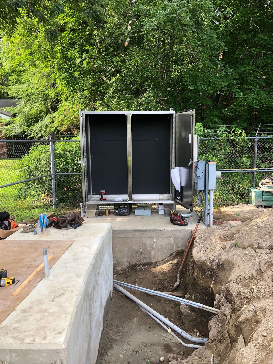 A stainless steel box is sitting on top of a concrete wall next to a hole in the ground.