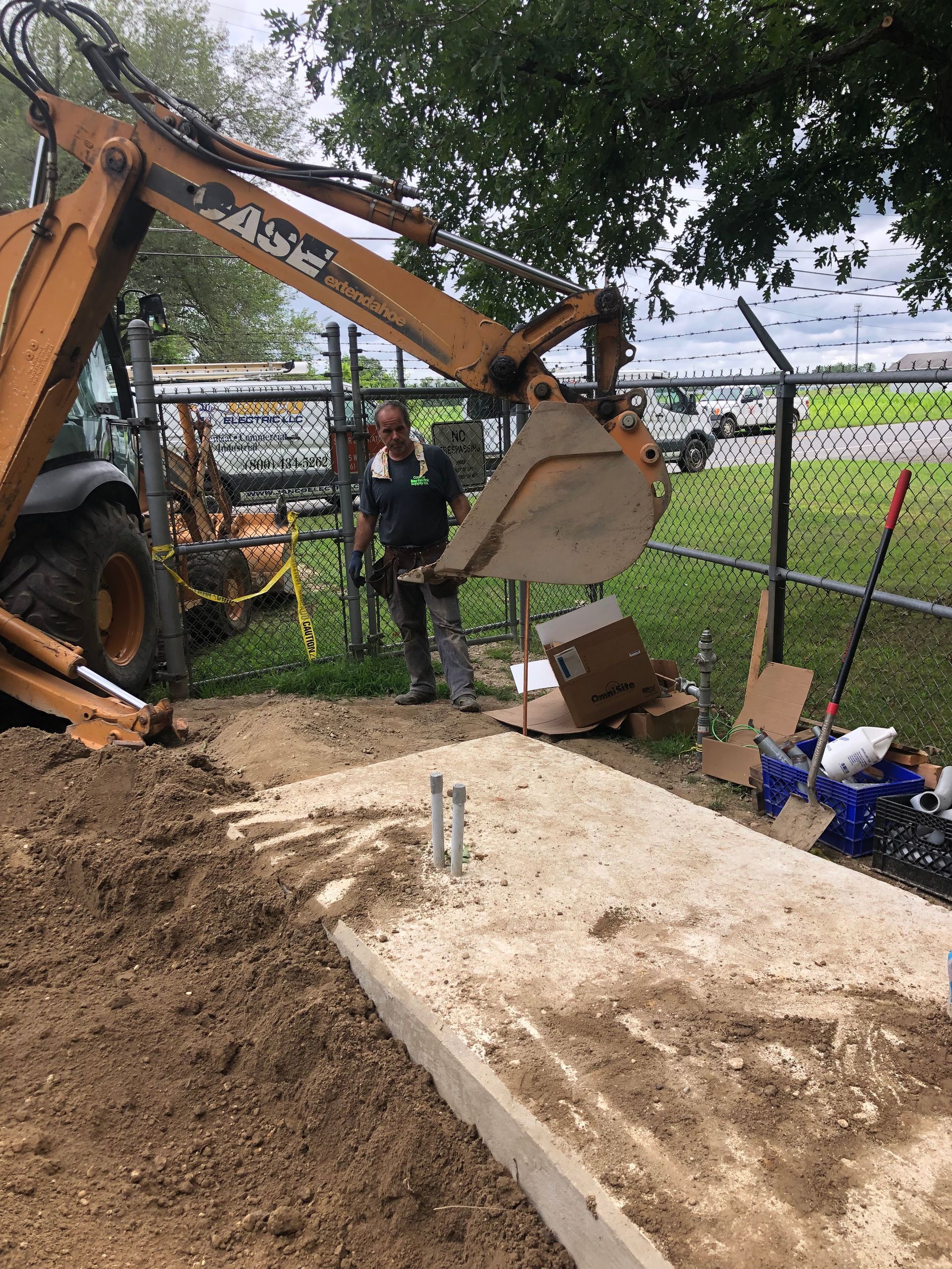 A man is standing next to a tractor digging a hole in the ground.