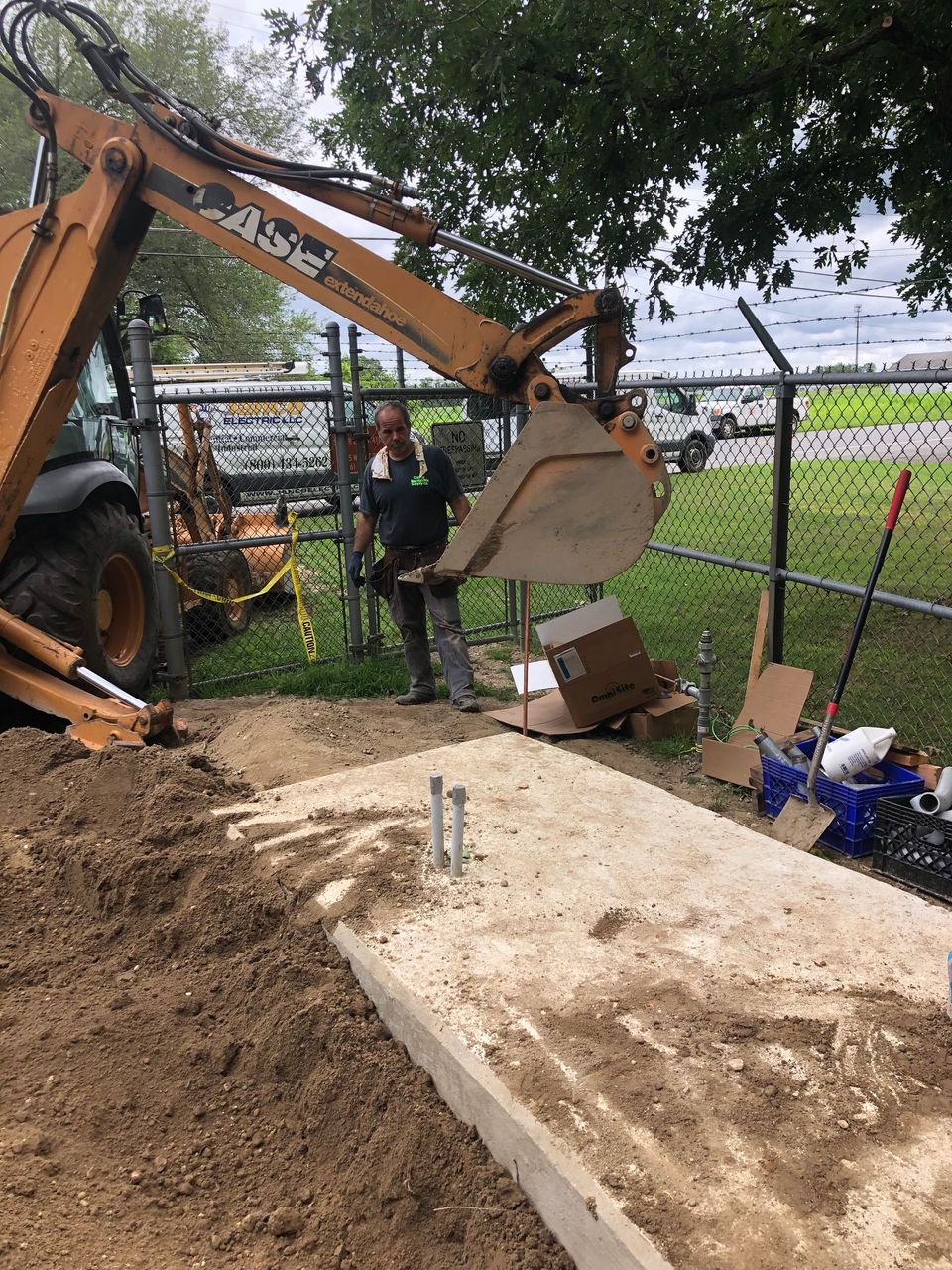 A man is standing next to a tractor digging a hole in the ground.