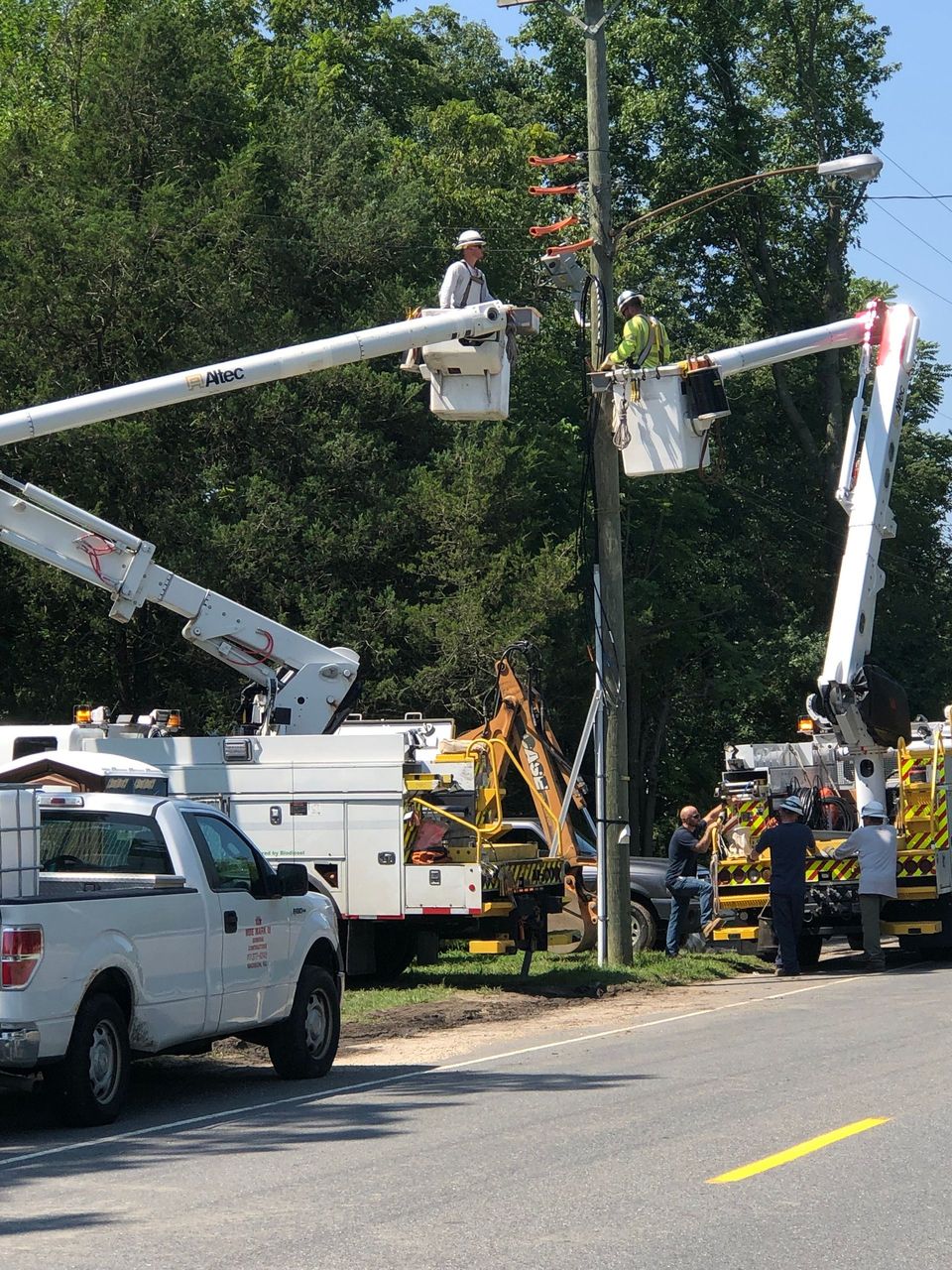 A white truck is parked on the side of the road next to a crane.