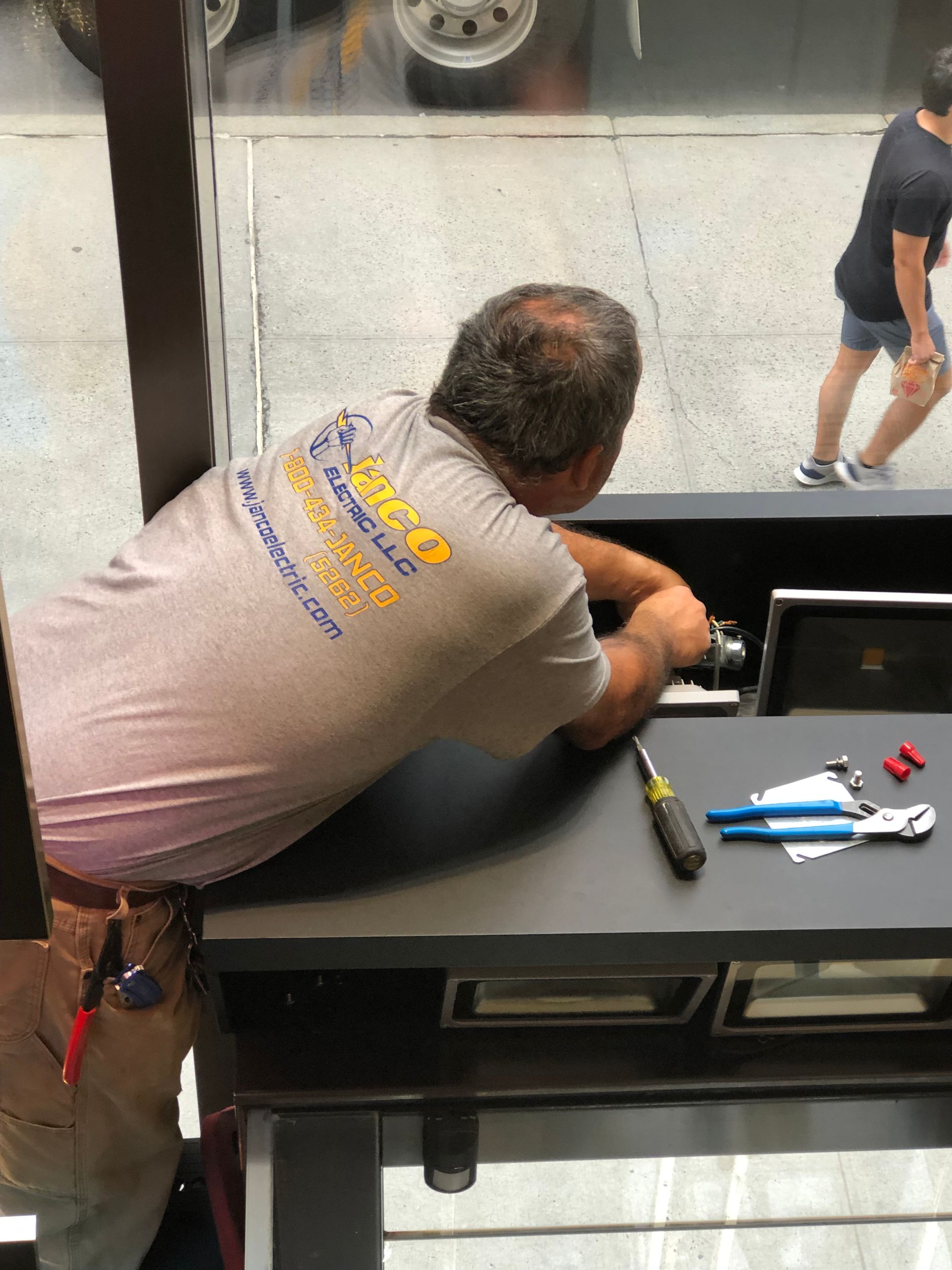 A man is sitting at a desk with tools on it and a shirt that says ' quick ' on the back