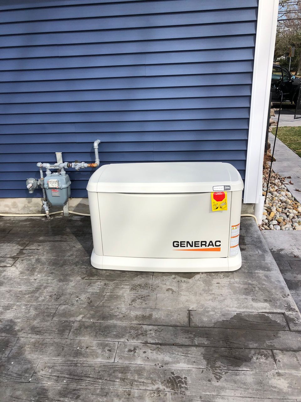 A generator is sitting in front of a blue house.