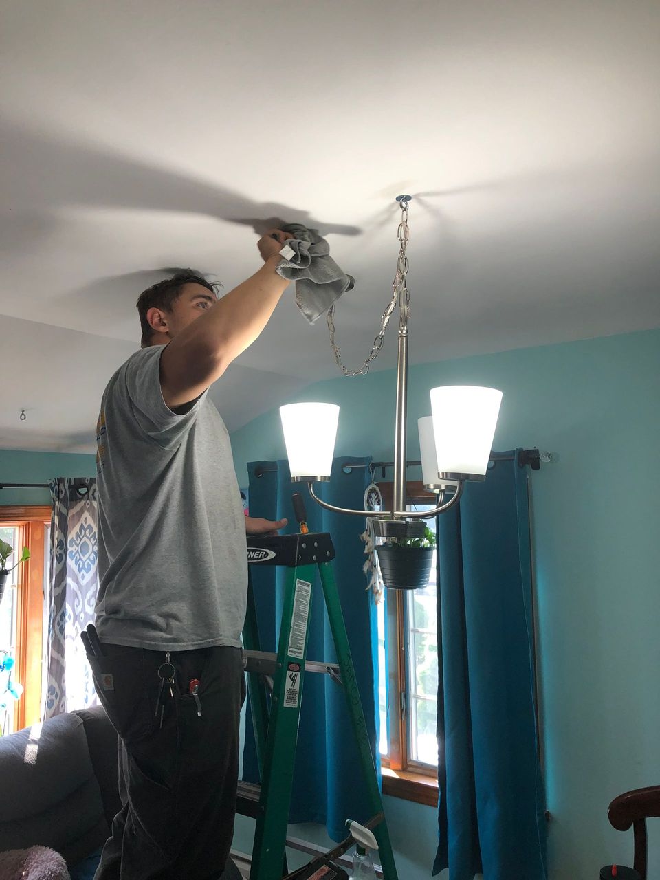 A man is working on a chandelier in a living room.
