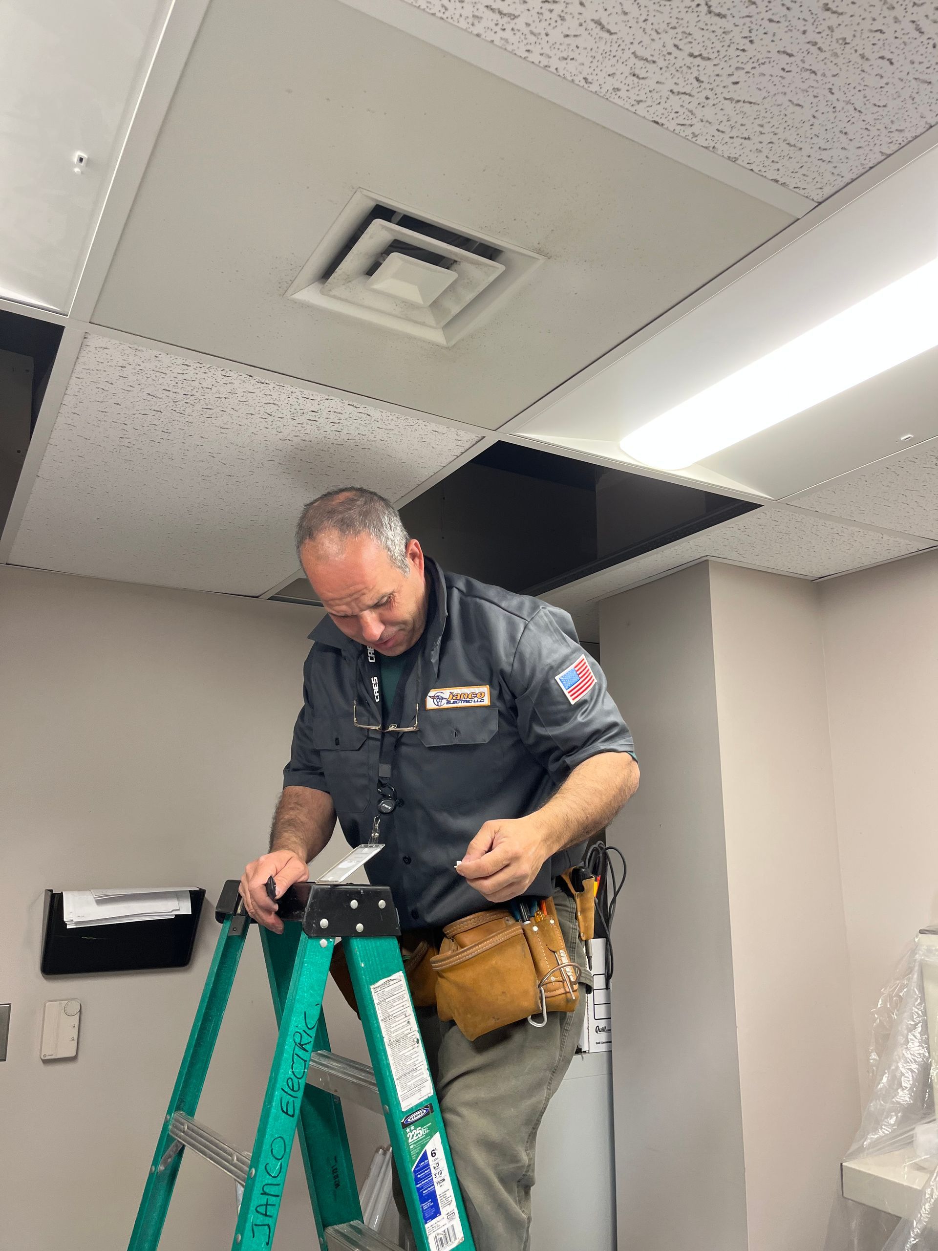 A man is standing on a ladder working on a ceiling.