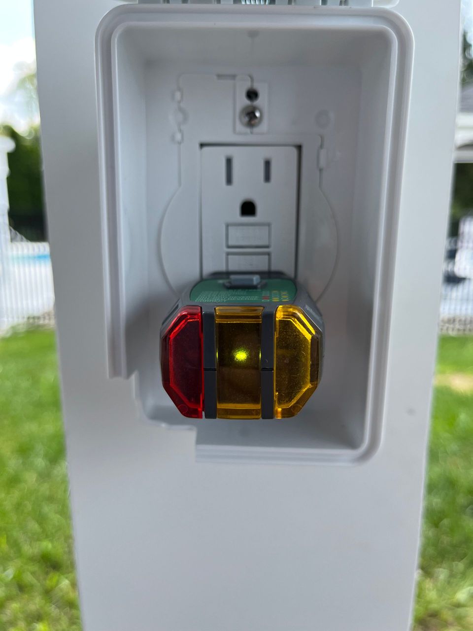 A white electrical outlet with a red and yellow light on it.