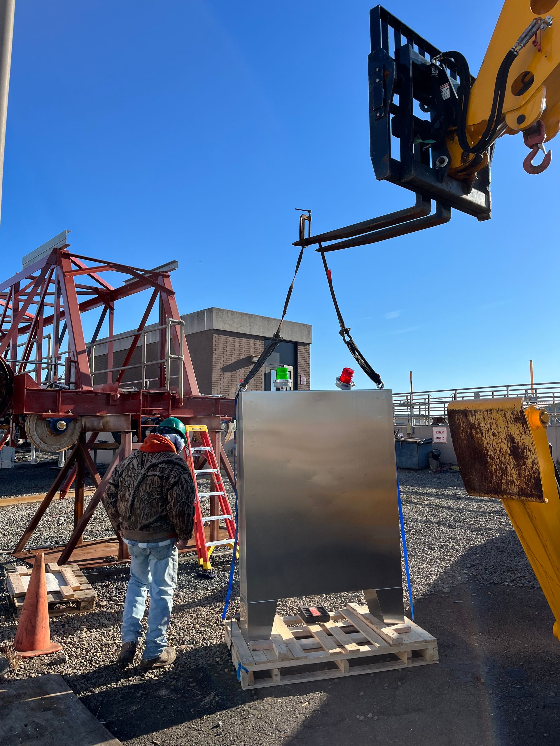 A crane is lifting a stainless steel box on a pallet
