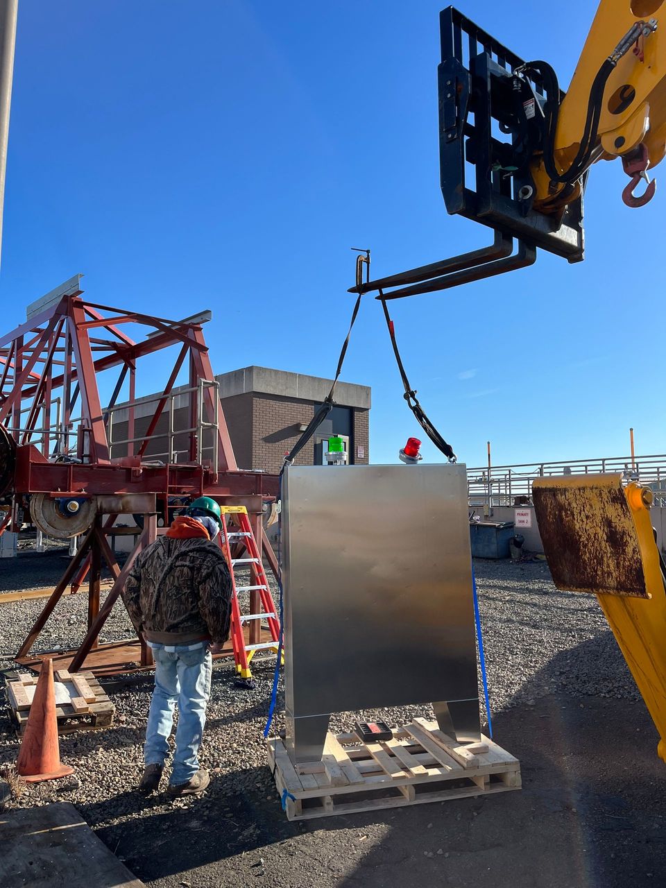 A crane is lifting a stainless steel box on a pallet