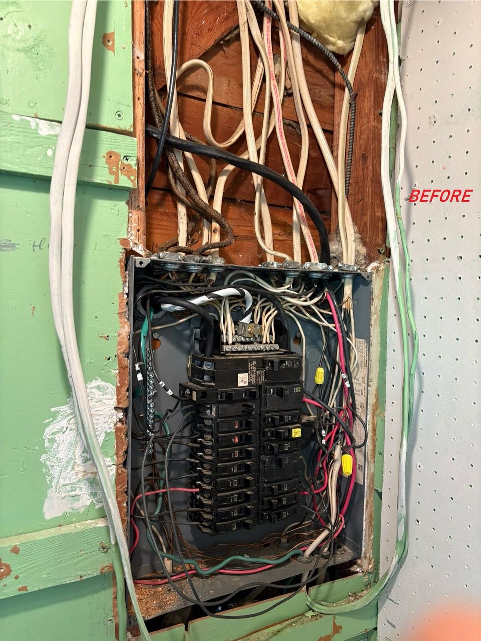 Open electrical breaker panel with exposed wires in a damaged wall opening