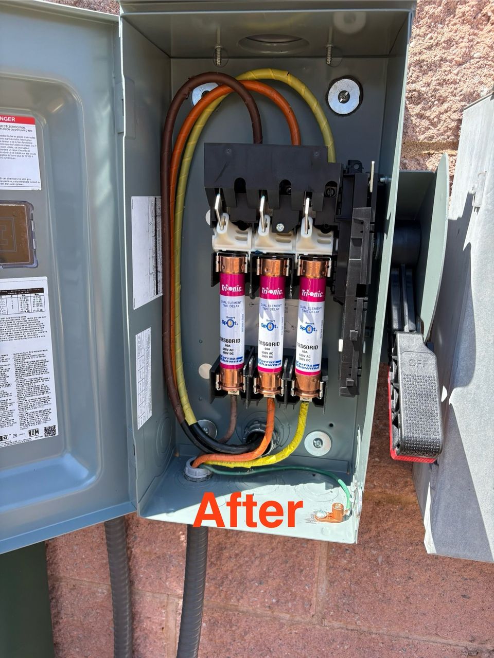 Open electrical panel with three fuses, labeled “After,” against a brick wall.