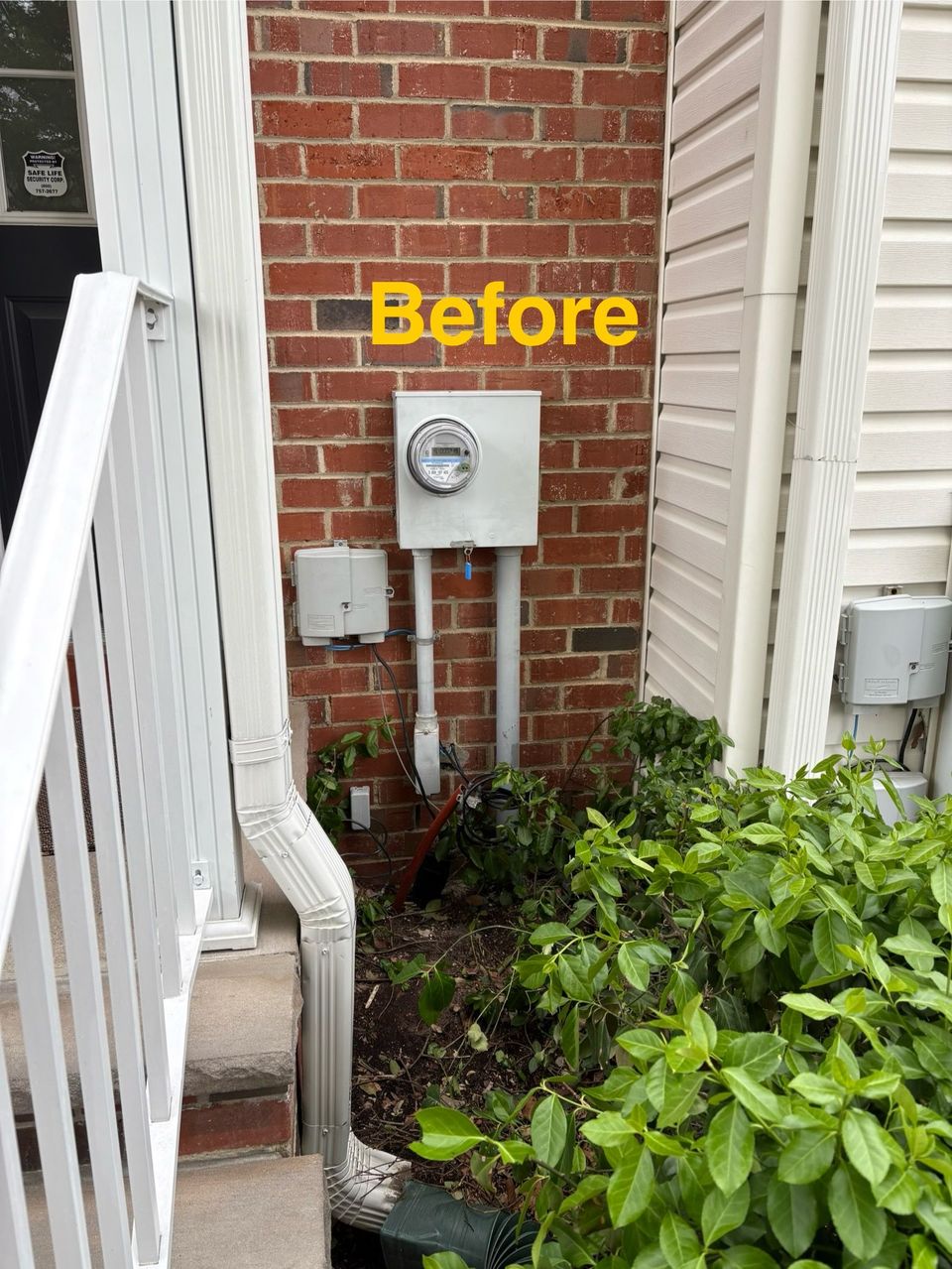 Brick wall with utility meter and pipes beside a white fence, labeled “Before” above greenery.