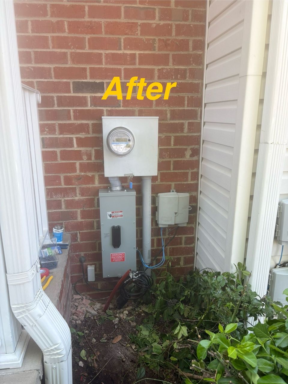 After: utility meters on a brick wall beside white downspouts and overgrown plants