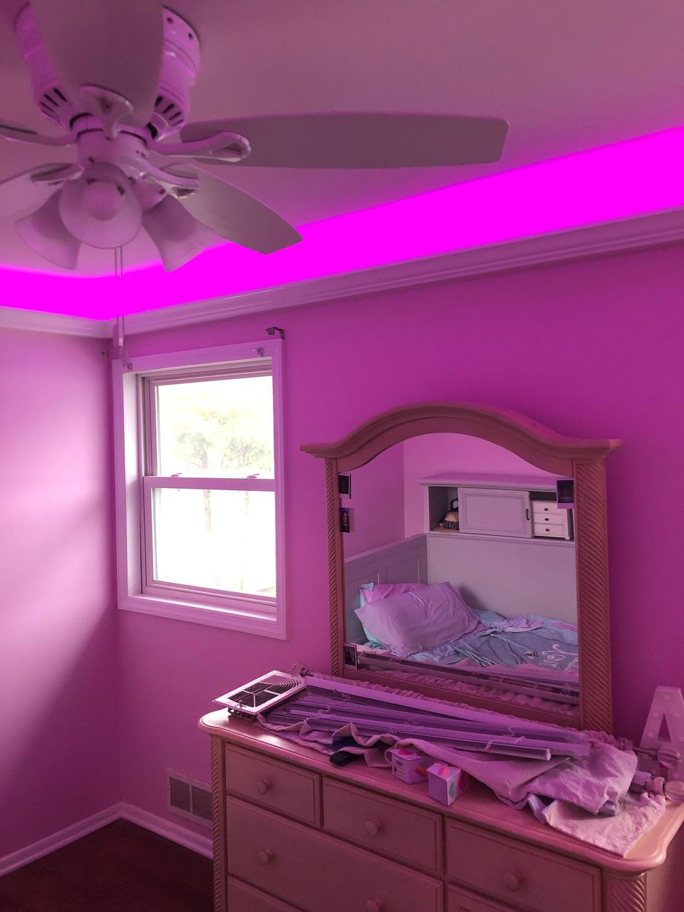 A bedroom with pink walls , a dresser , a mirror and a ceiling fan.