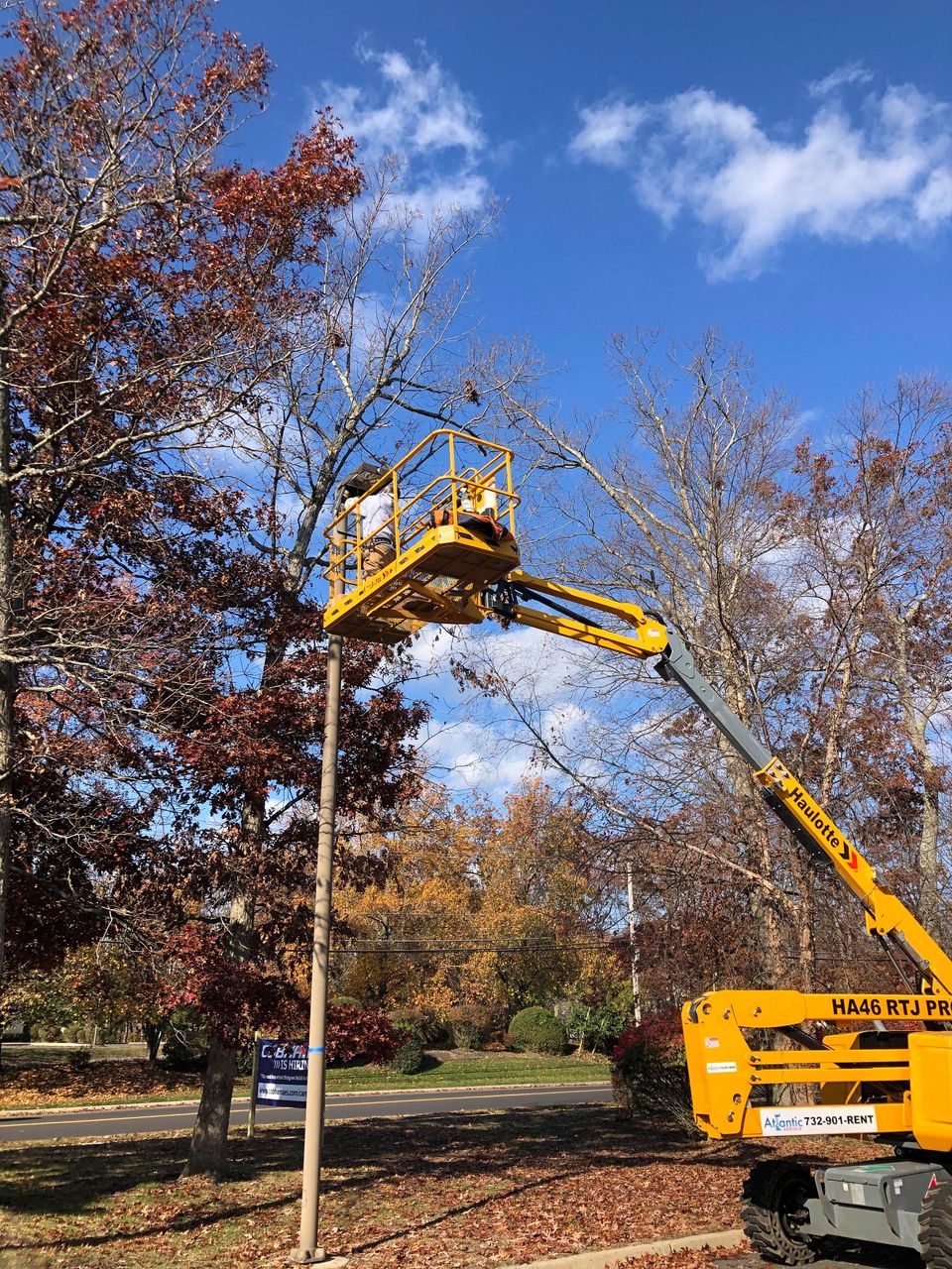 A man is standing in a bucket on top of a yellow crane.