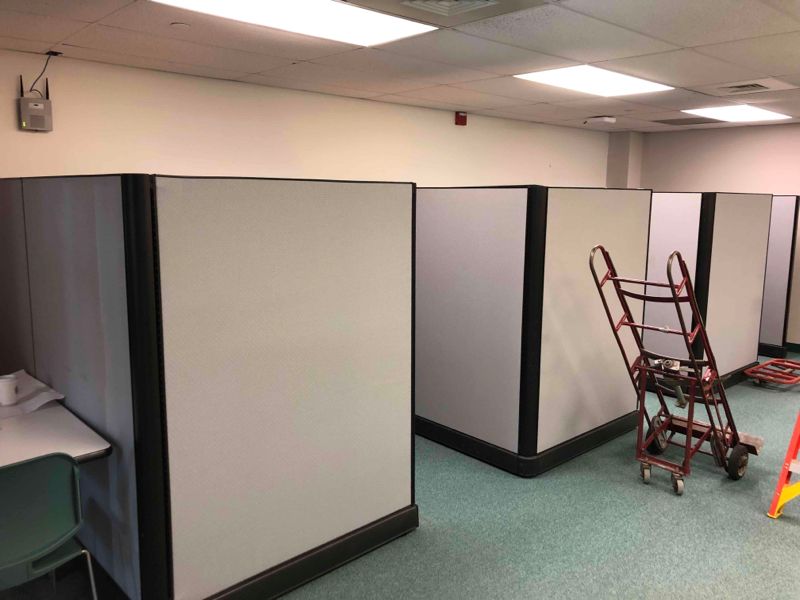 Office cubicles with gray partitions, green carpet, and a hand truck in the aisle.