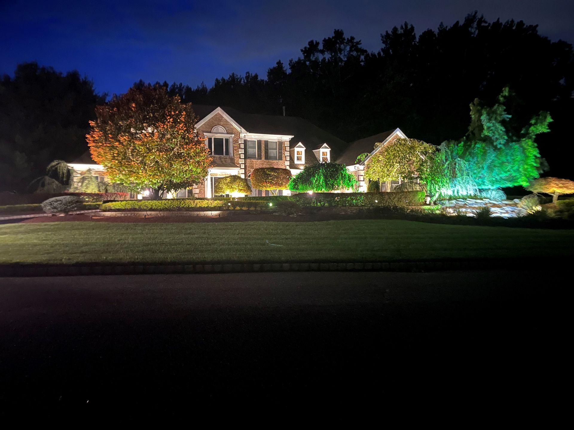 A large house is lit up at night with trees in the background