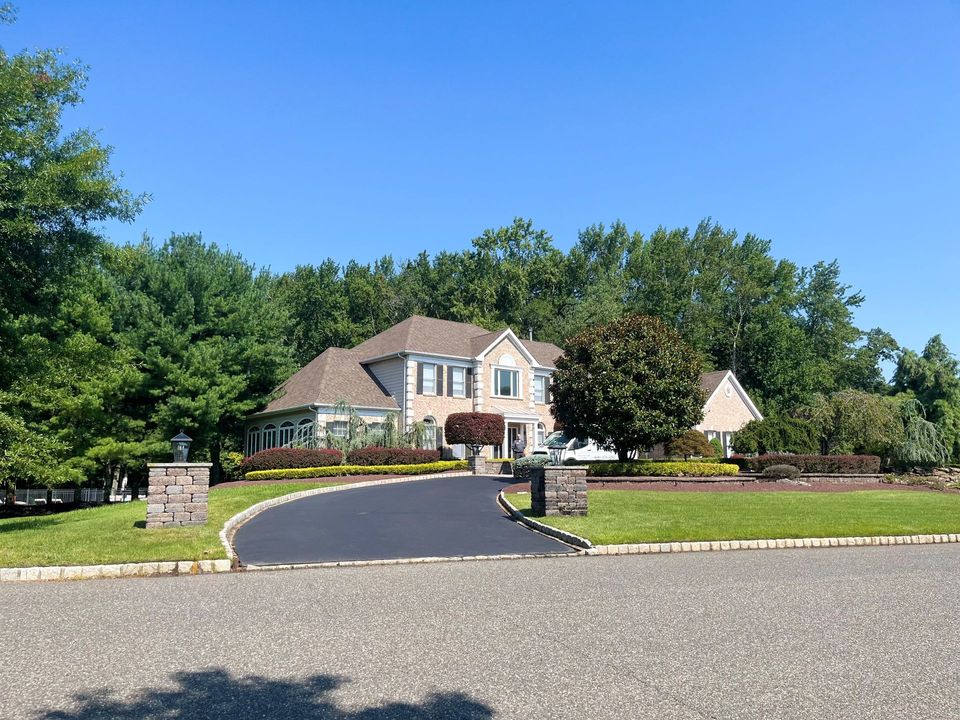 A large house with a driveway leading to it is surrounded by trees.