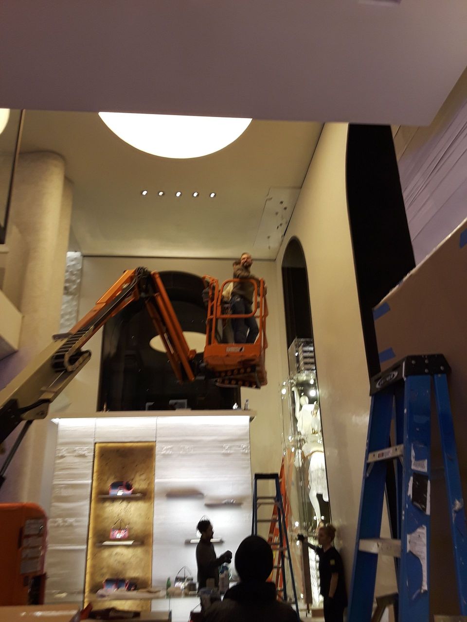 A man on a lift in a room with a ladder in the foreground