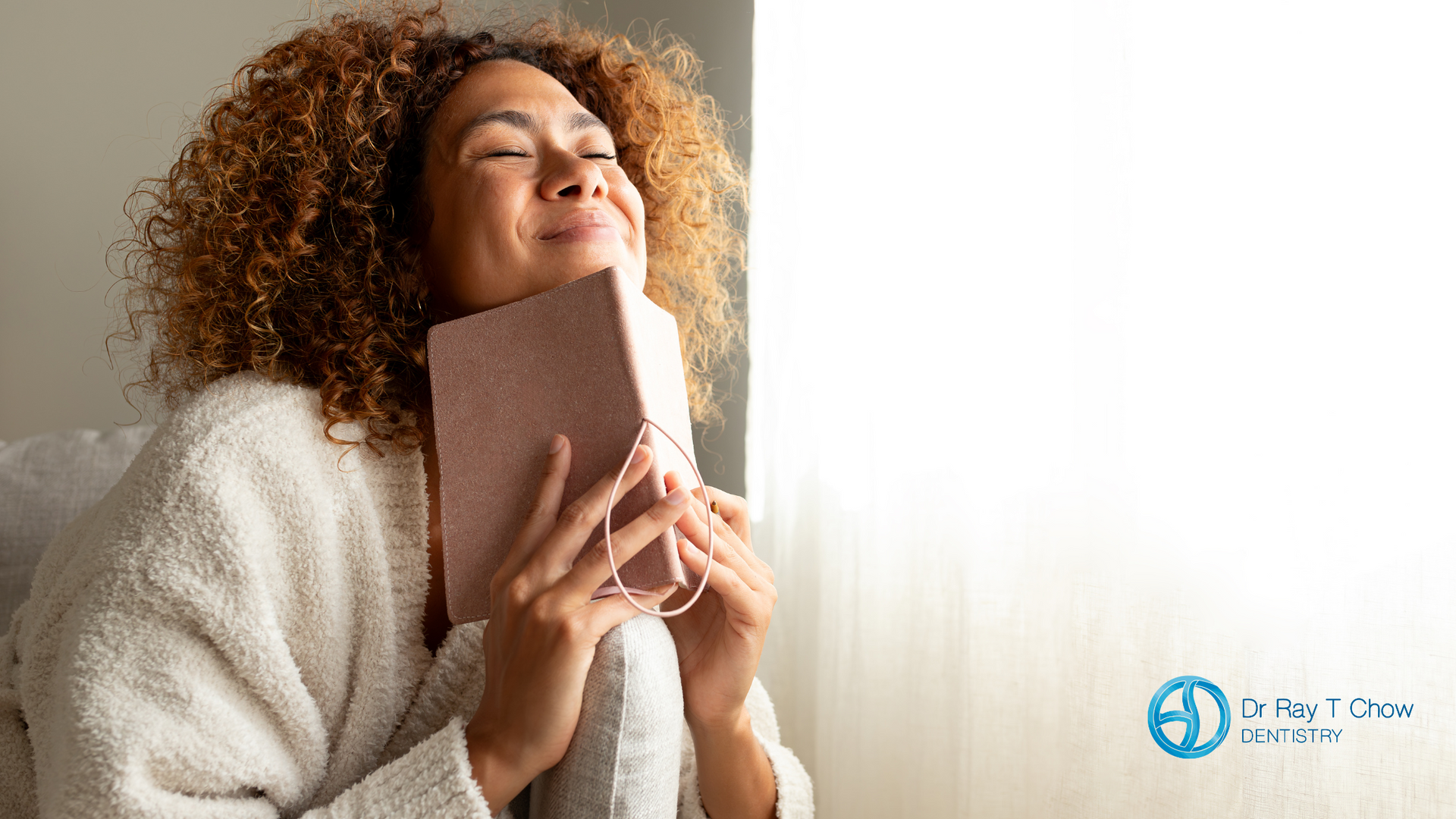 A woman is sitting on a bed with her eyes closed and holding a book.