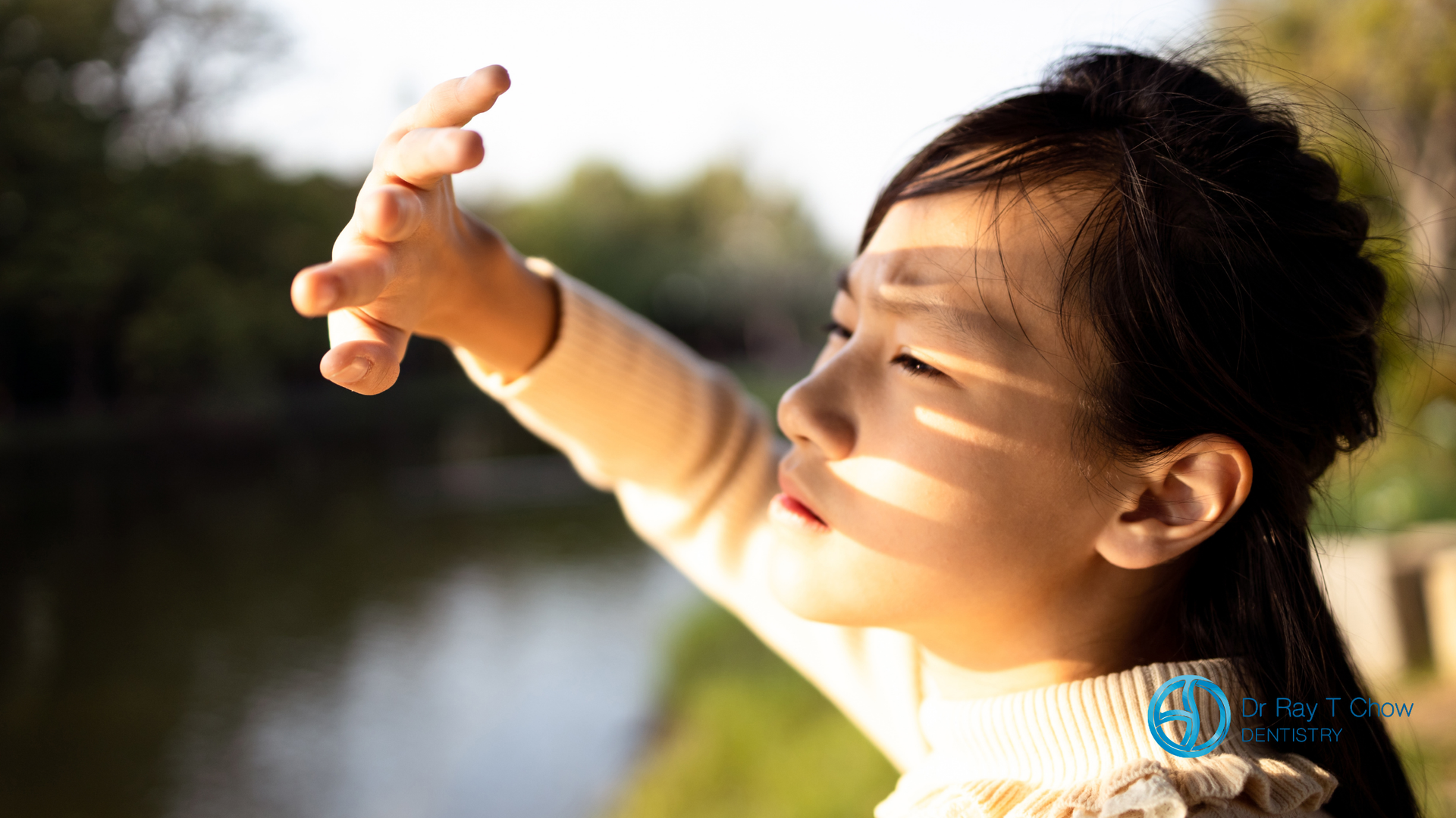 A little girl is covering her face from the sun with her hands.