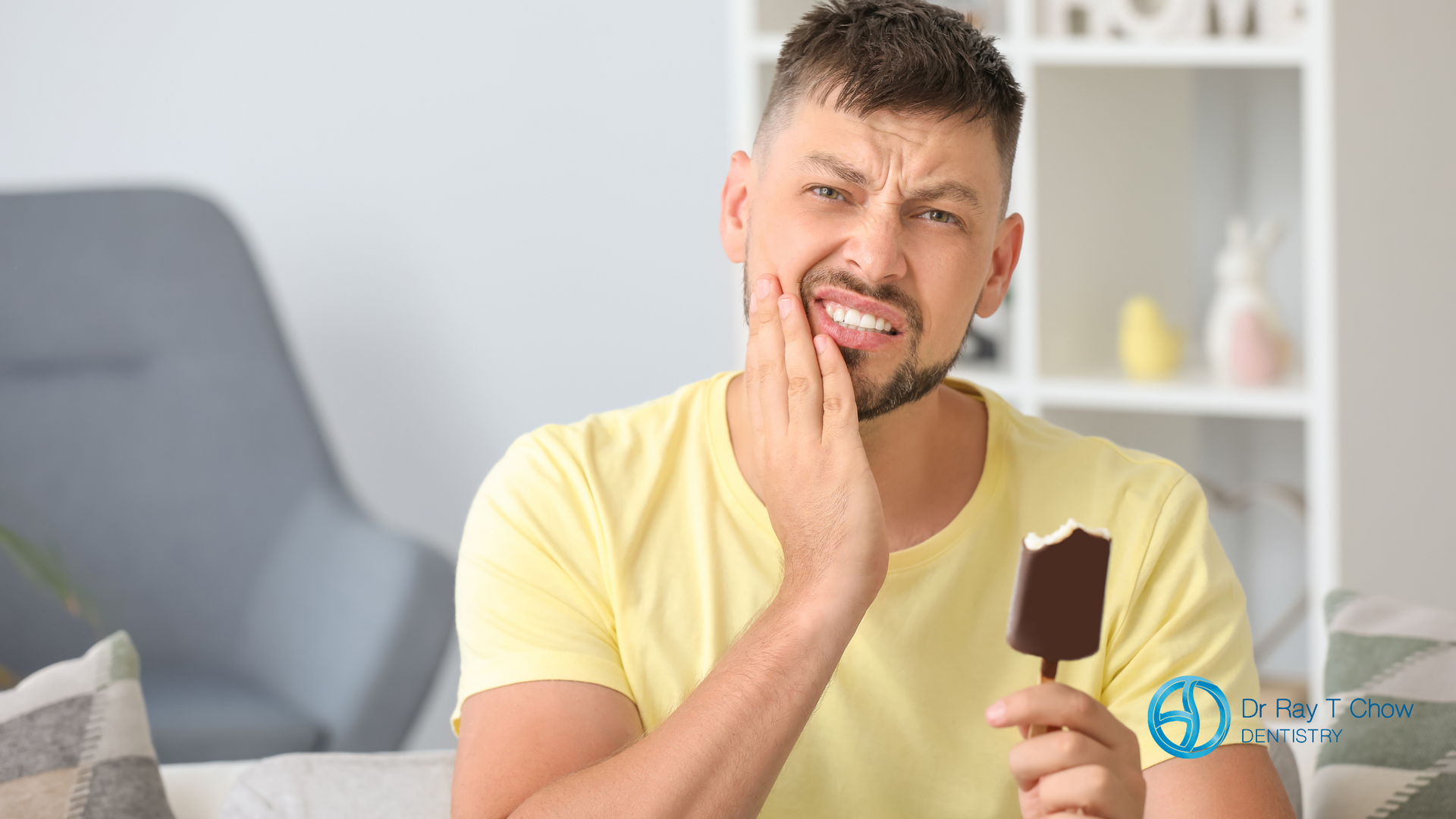 A man is holding an ice cream bar in his hand and has a toothache.