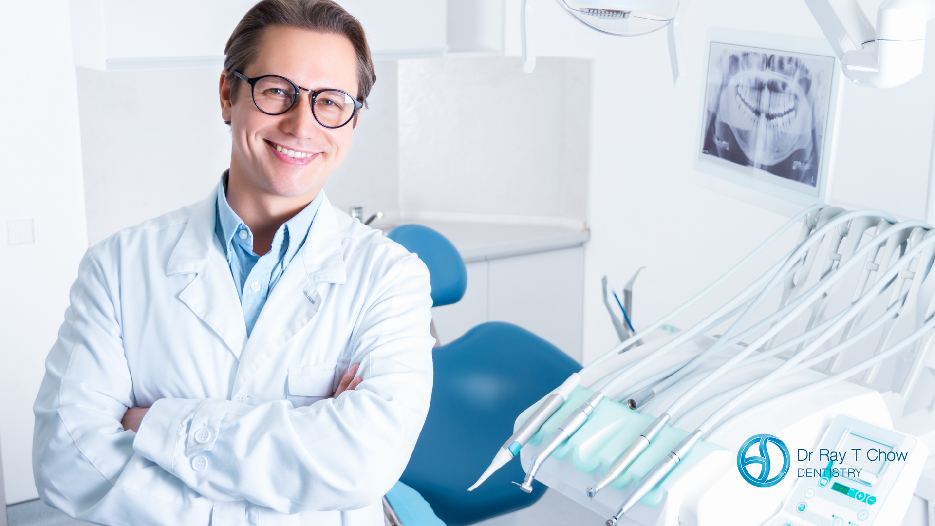 A dentist is smiling in a dental office with his arms crossed.