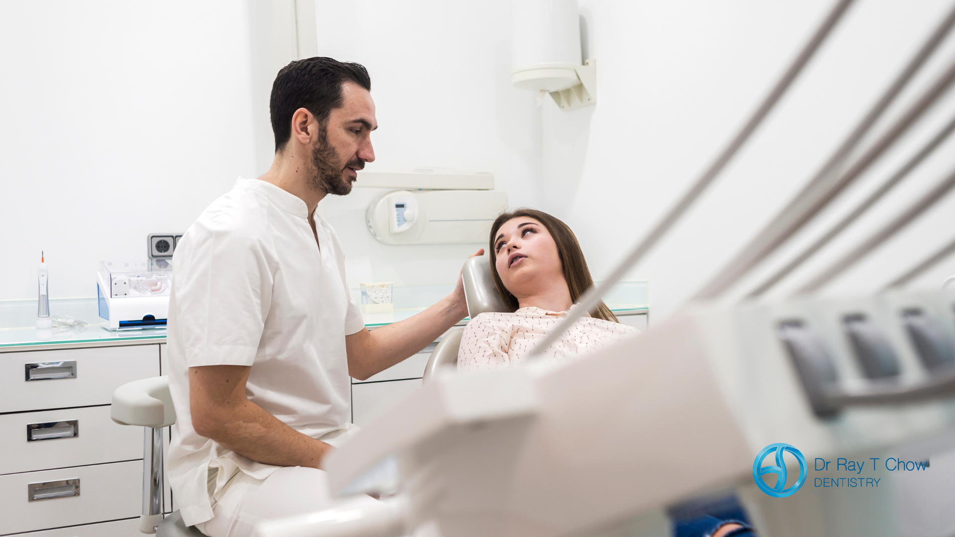 A dentist is talking to a patient in a dental chair.