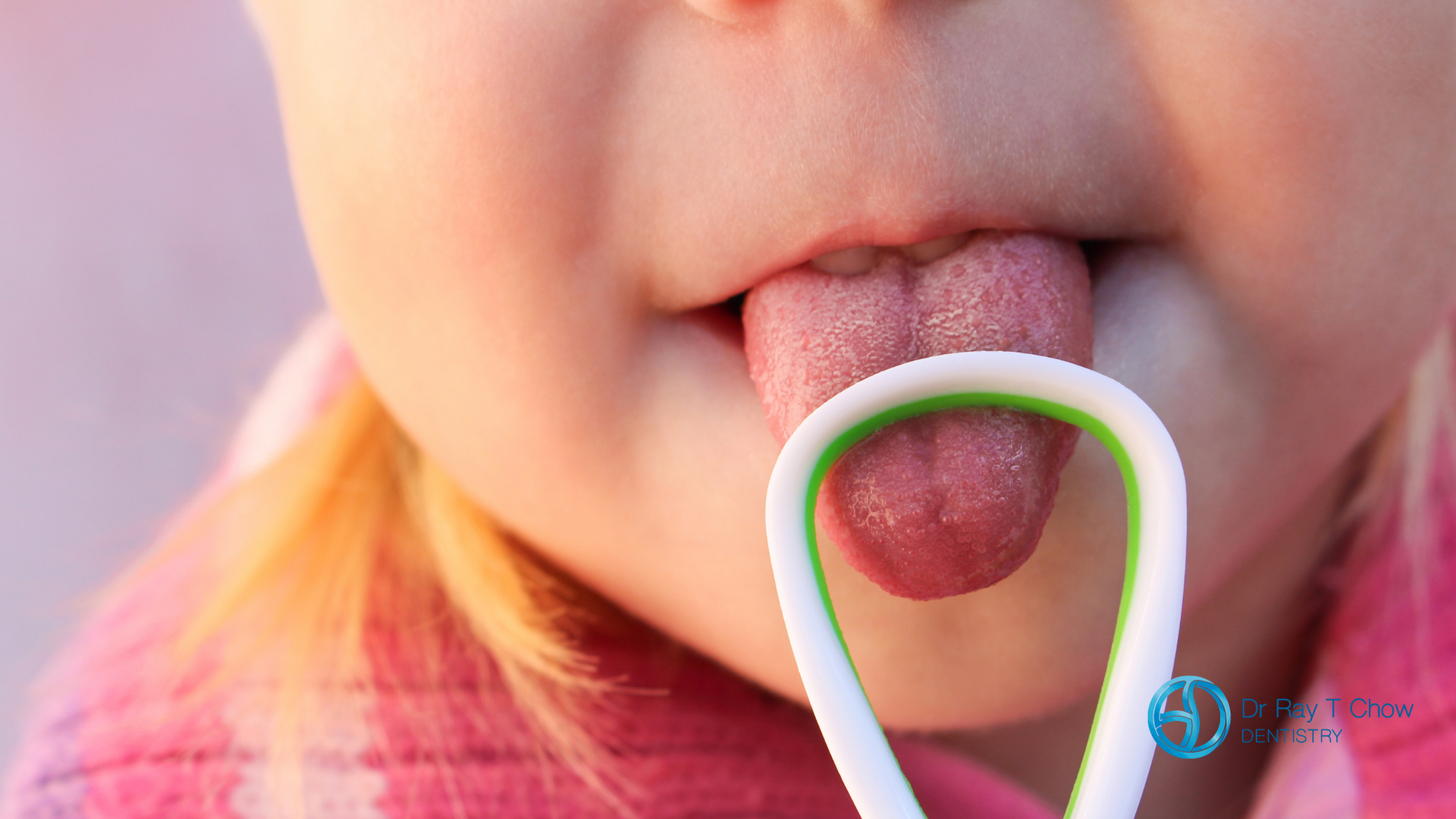 A little girl is sticking her tongue out while holding a spoon in her mouth.