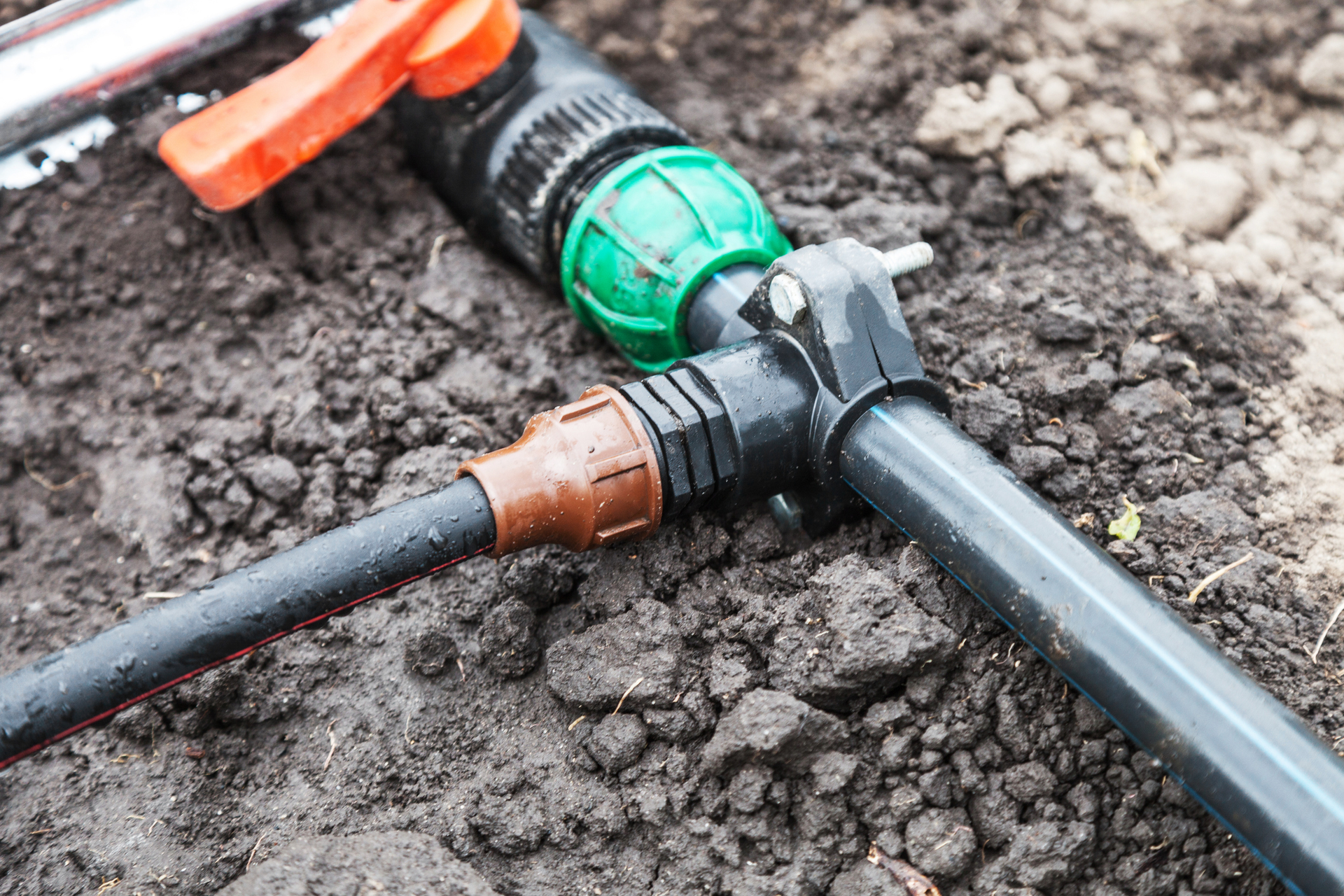 A close up of a hose connected to a sprinkler in the dirt.