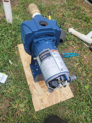 A blue water pump is sitting on a wooden board in the grass.