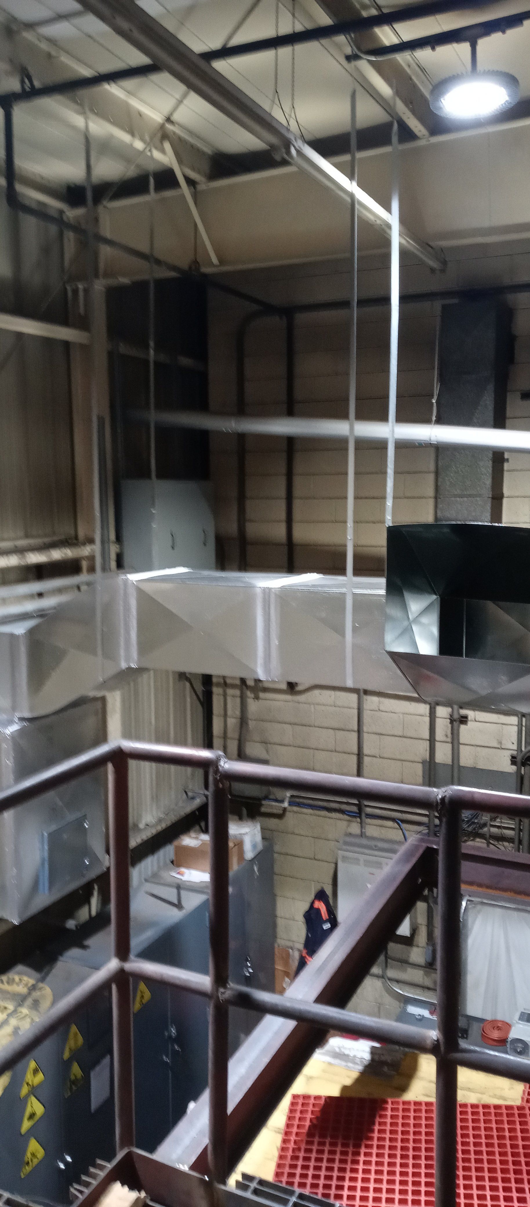 View of an industrial interior with ventilation ducts, metal railing, and a person in the background.