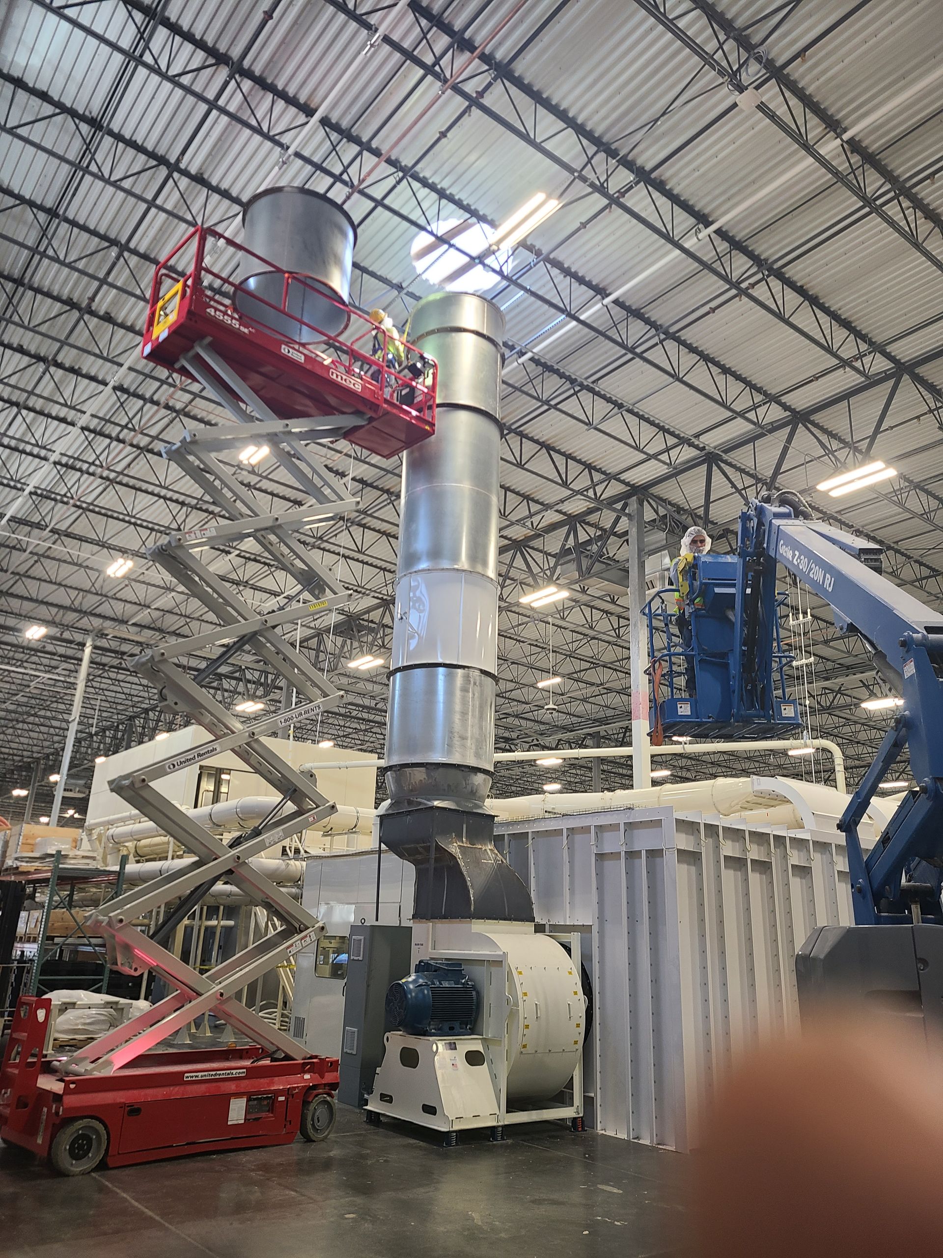 Workers on lifts install ventilation stack in a large warehouse.