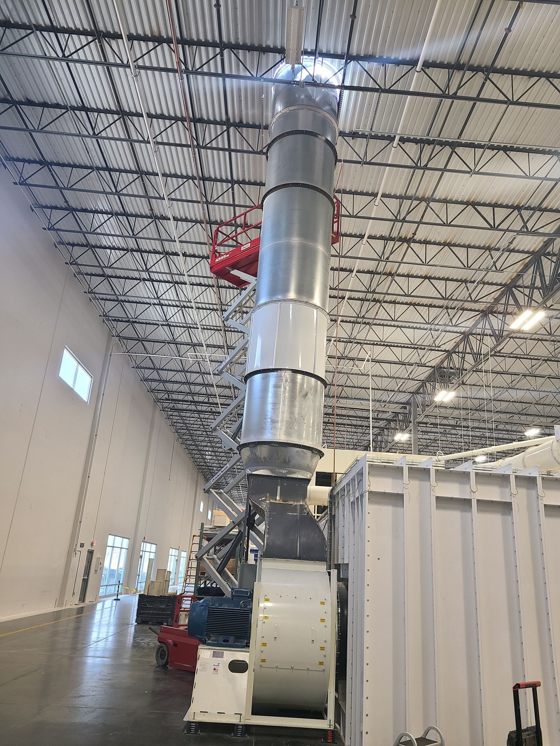 Large industrial exhaust system inside a building with a red lift and open bay doors.