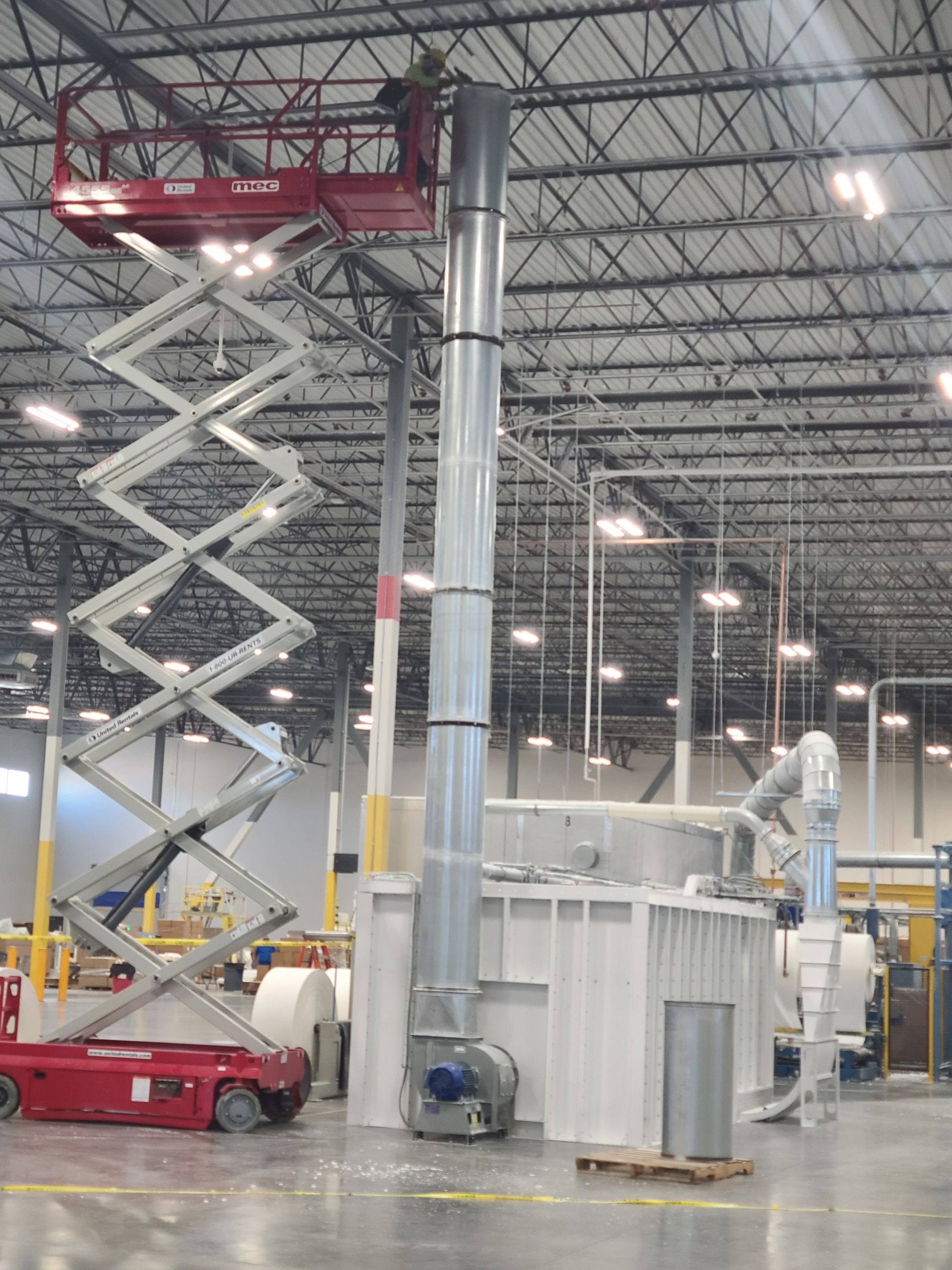 Person on scissor lift working on industrial exhaust stack in a factory setting.