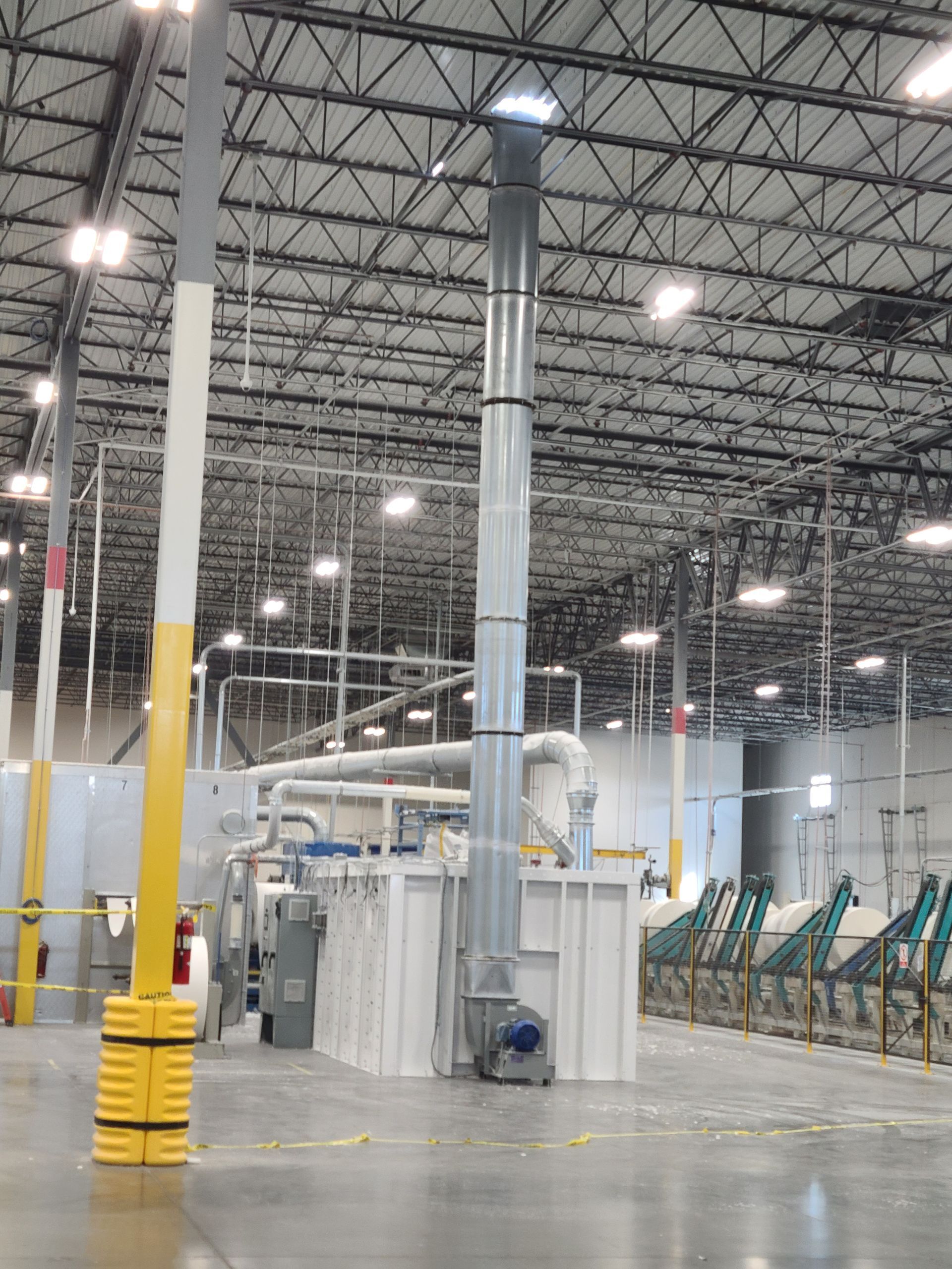 Large industrial facility interior. Ductwork extends up to the ceiling from a large, enclosed unit.