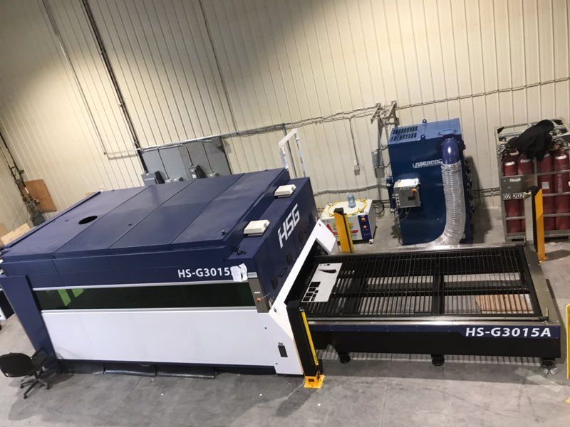 Blue and white HS-G3015 laser cutting machine in a factory setting.