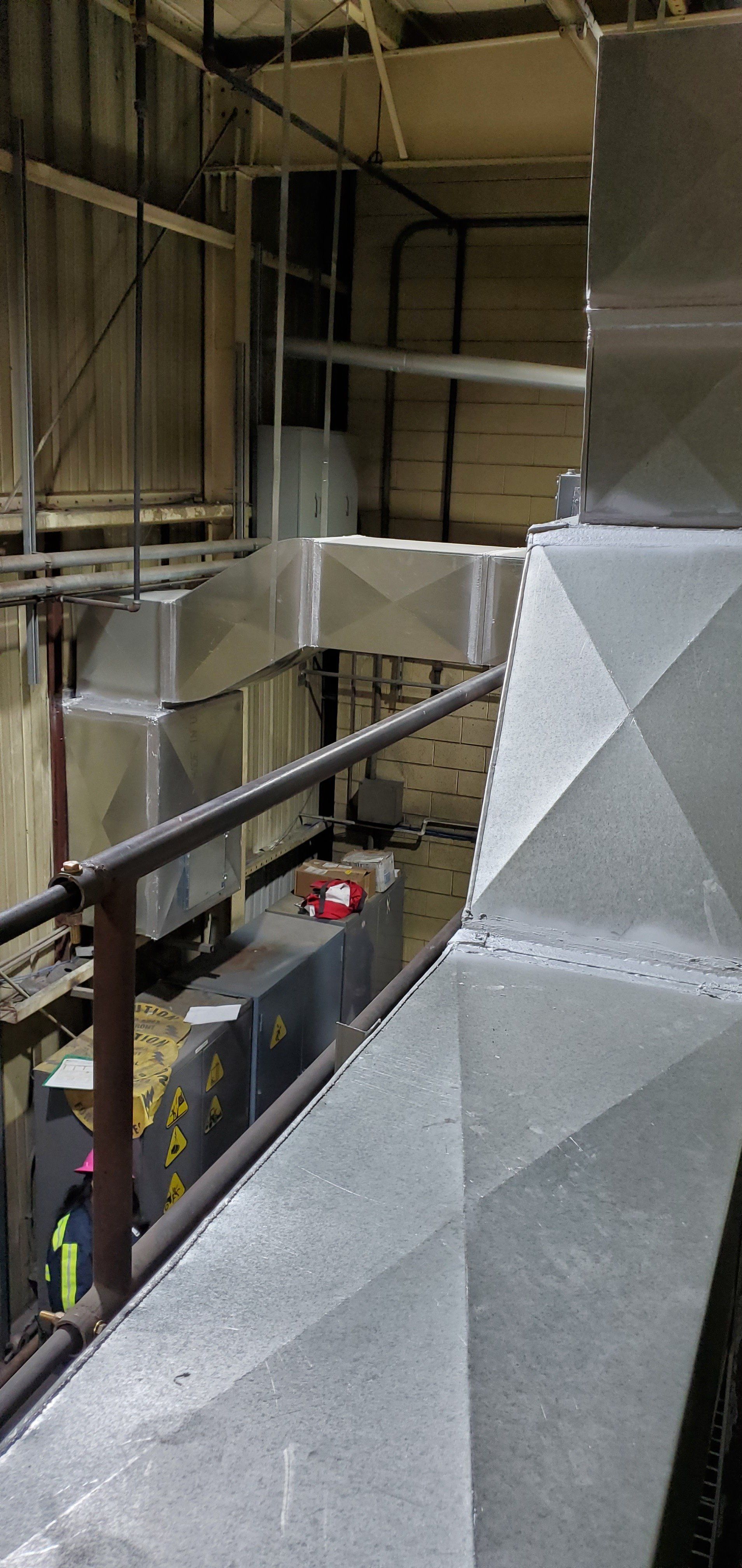 Large industrial ventilation system with metal ductwork, partially viewable in a factory setting.