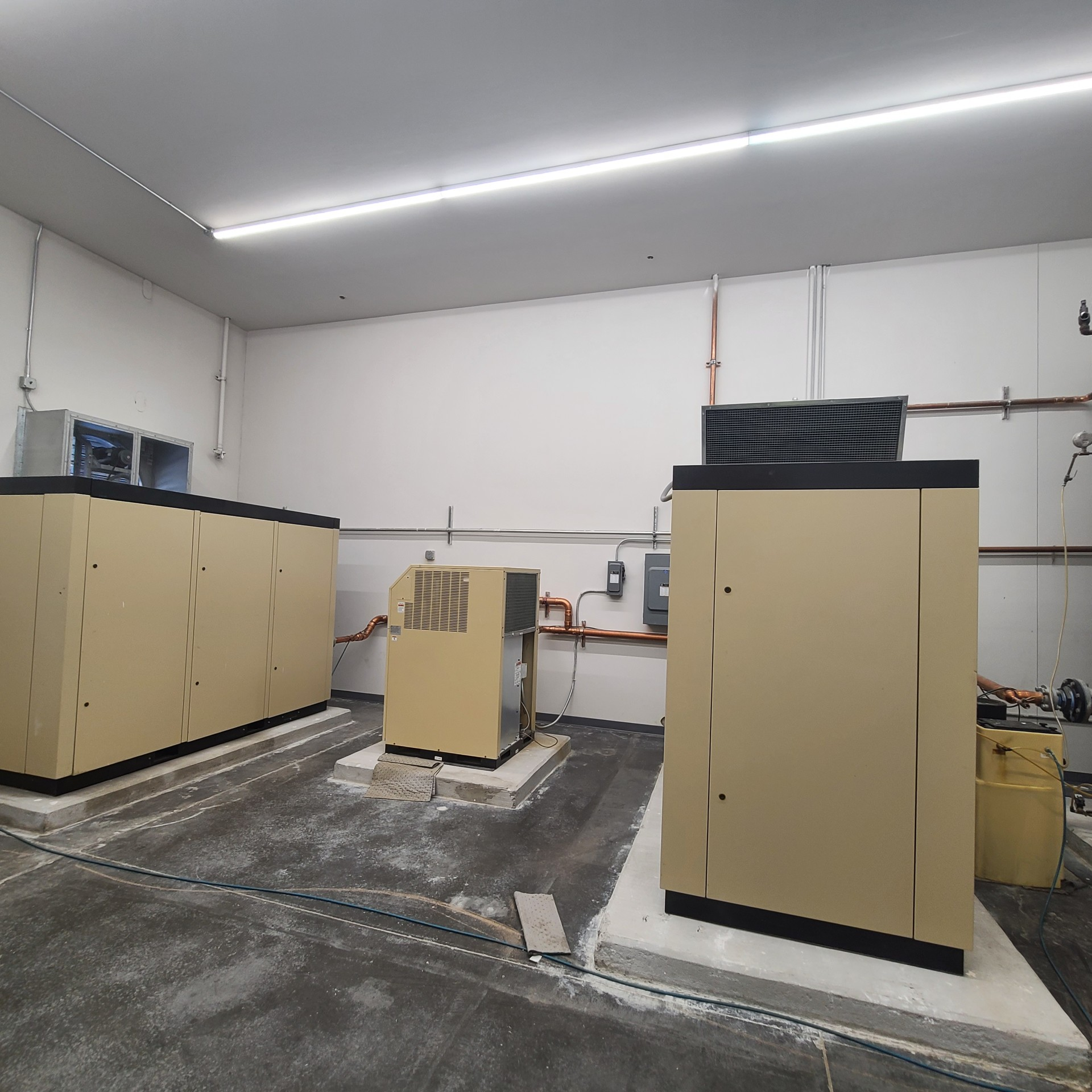 Three beige industrial machines in a white room with a concrete floor.