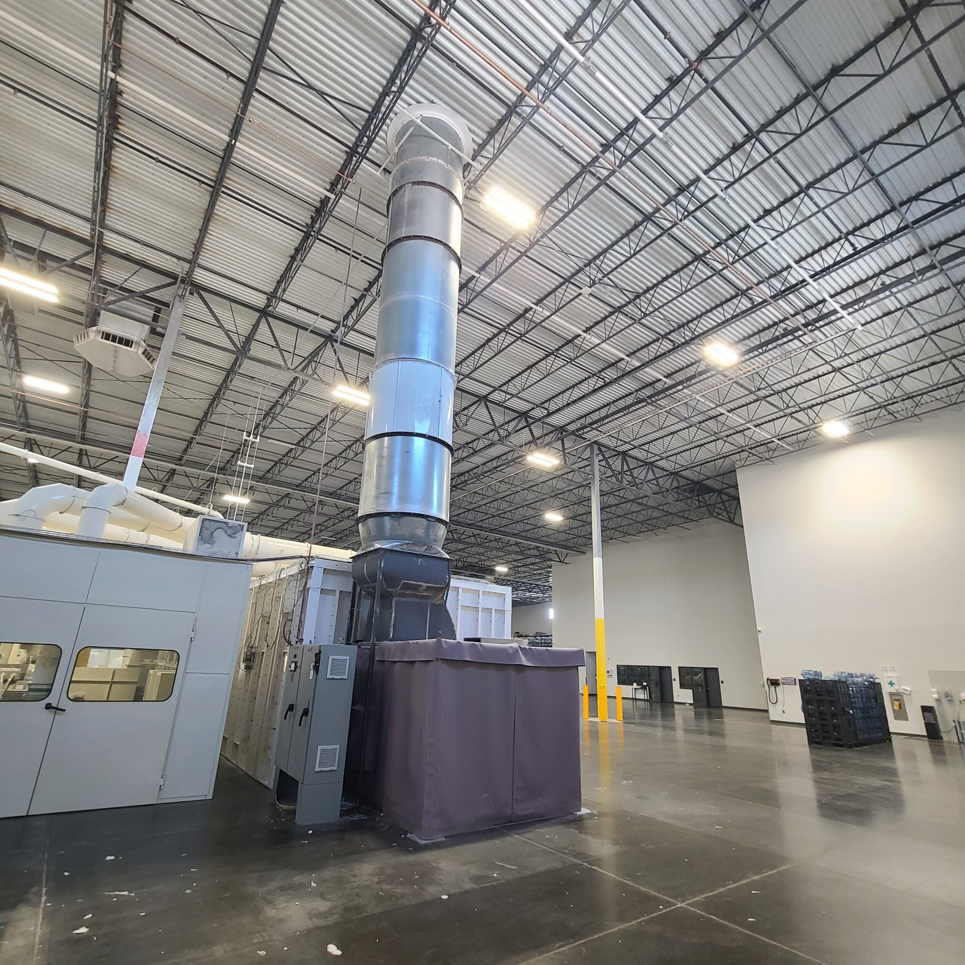 Industrial ventilation system inside a large warehouse. A tall, cylindrical chimney vents upward.